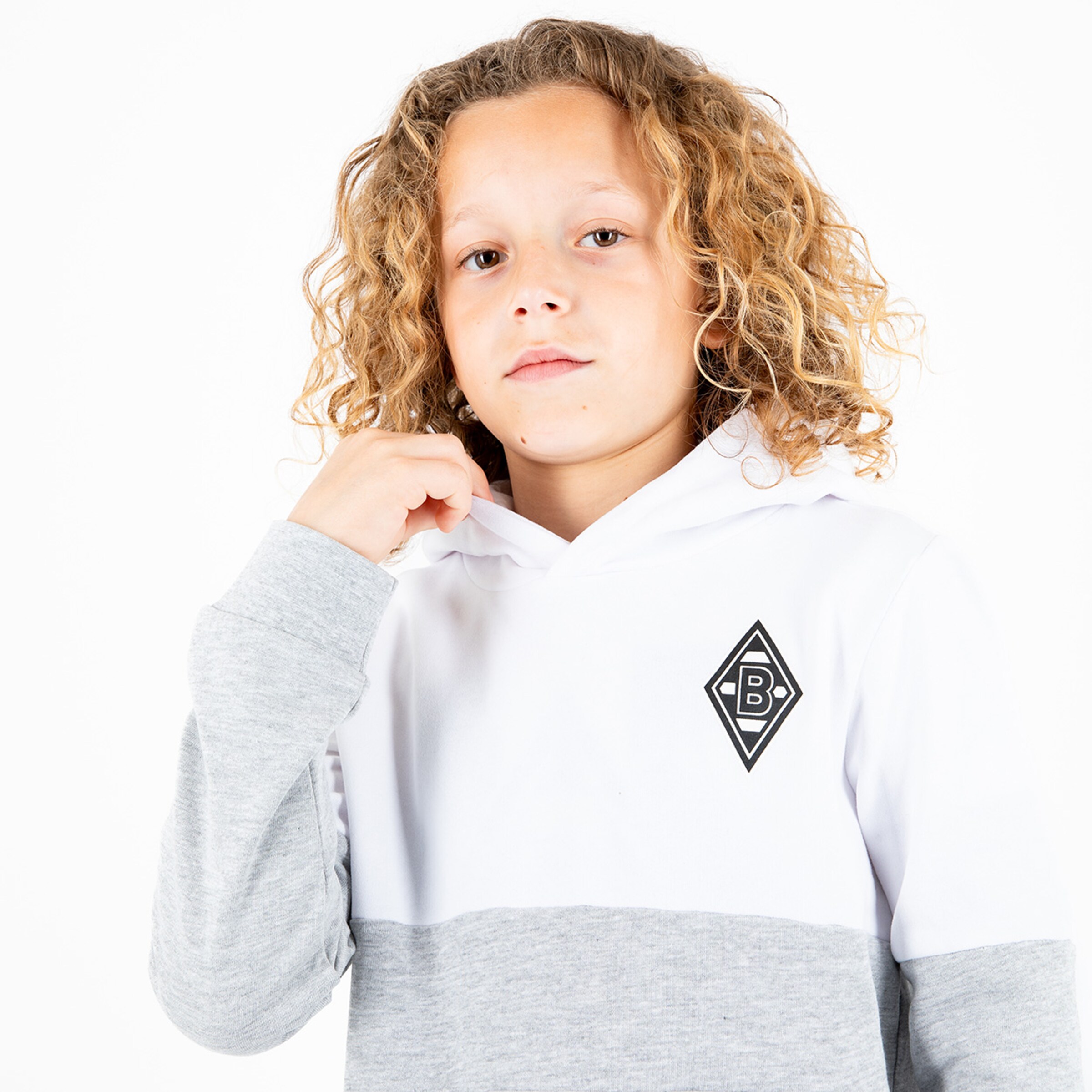 Ein Junge mit lockigem blonden Haar trägt einen grauen und weißen Hoodie mit dem Borussia Mönchengladbach Logo.