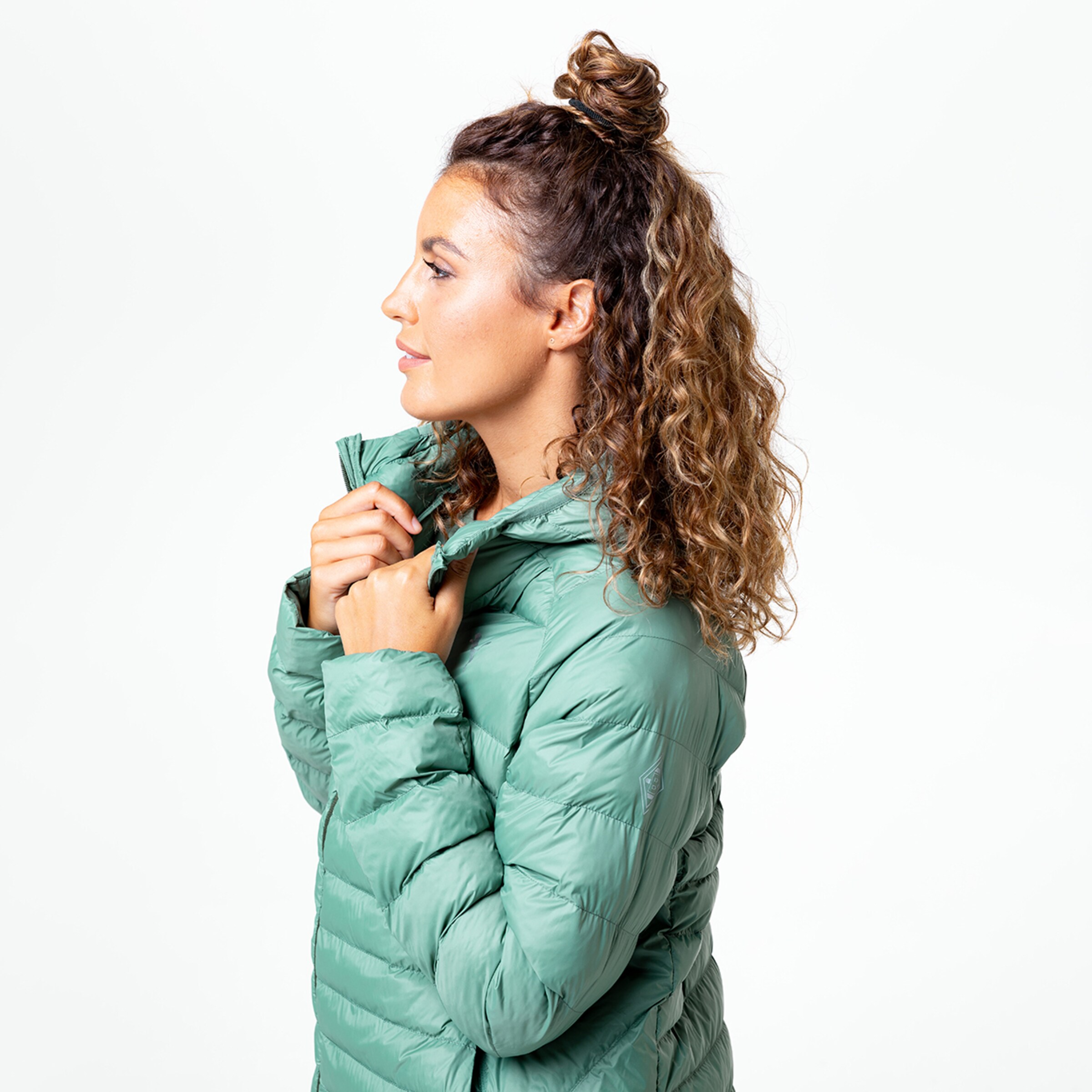 Frau mit lockigem Haar in einer grünen gefütterten Jacke seitliche Ansicht.
