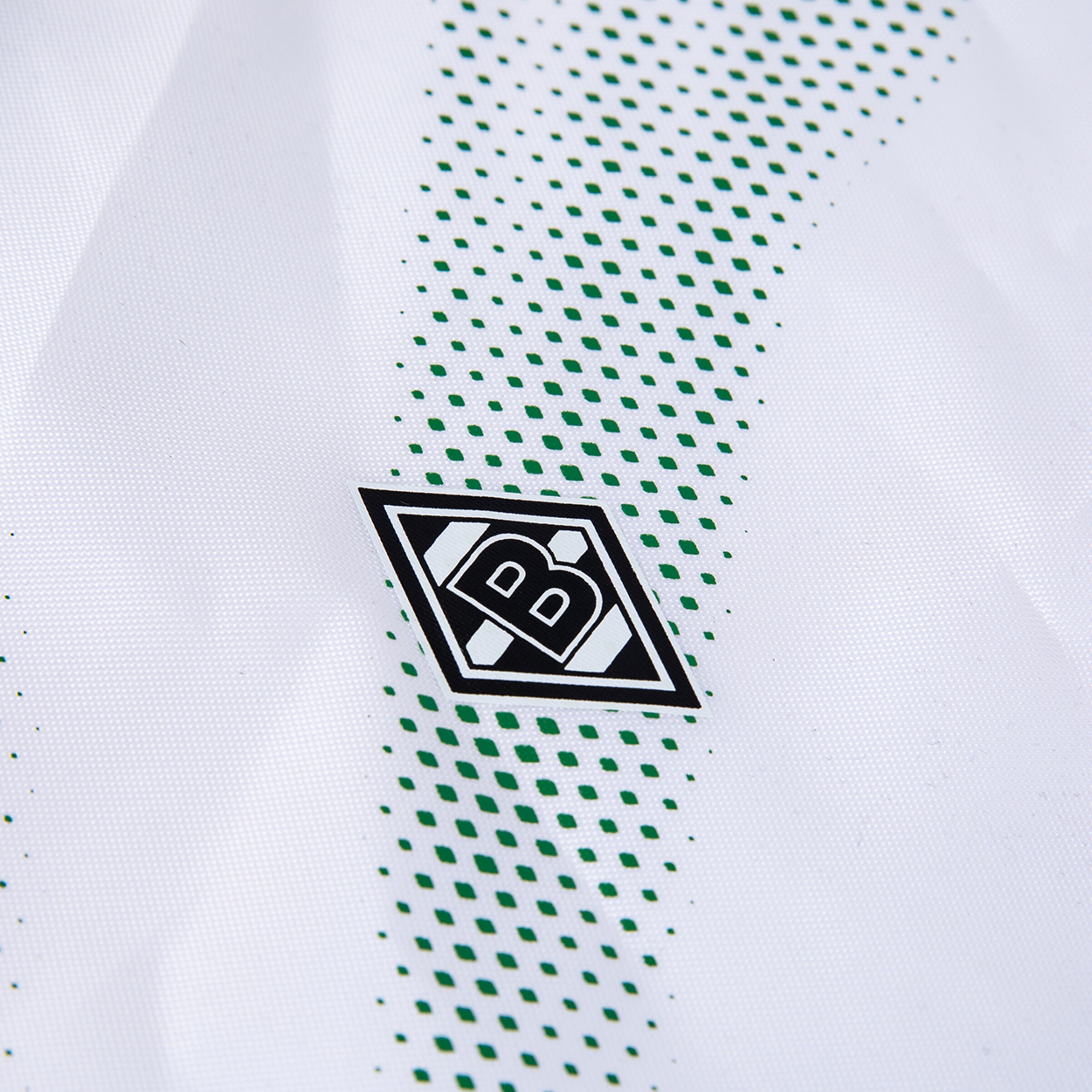 Nahaufnahme eines weißen Trikots mit grünem Rauten-Punktmuster und dem Vereinslogo von Borussia Mönchengladbach.
