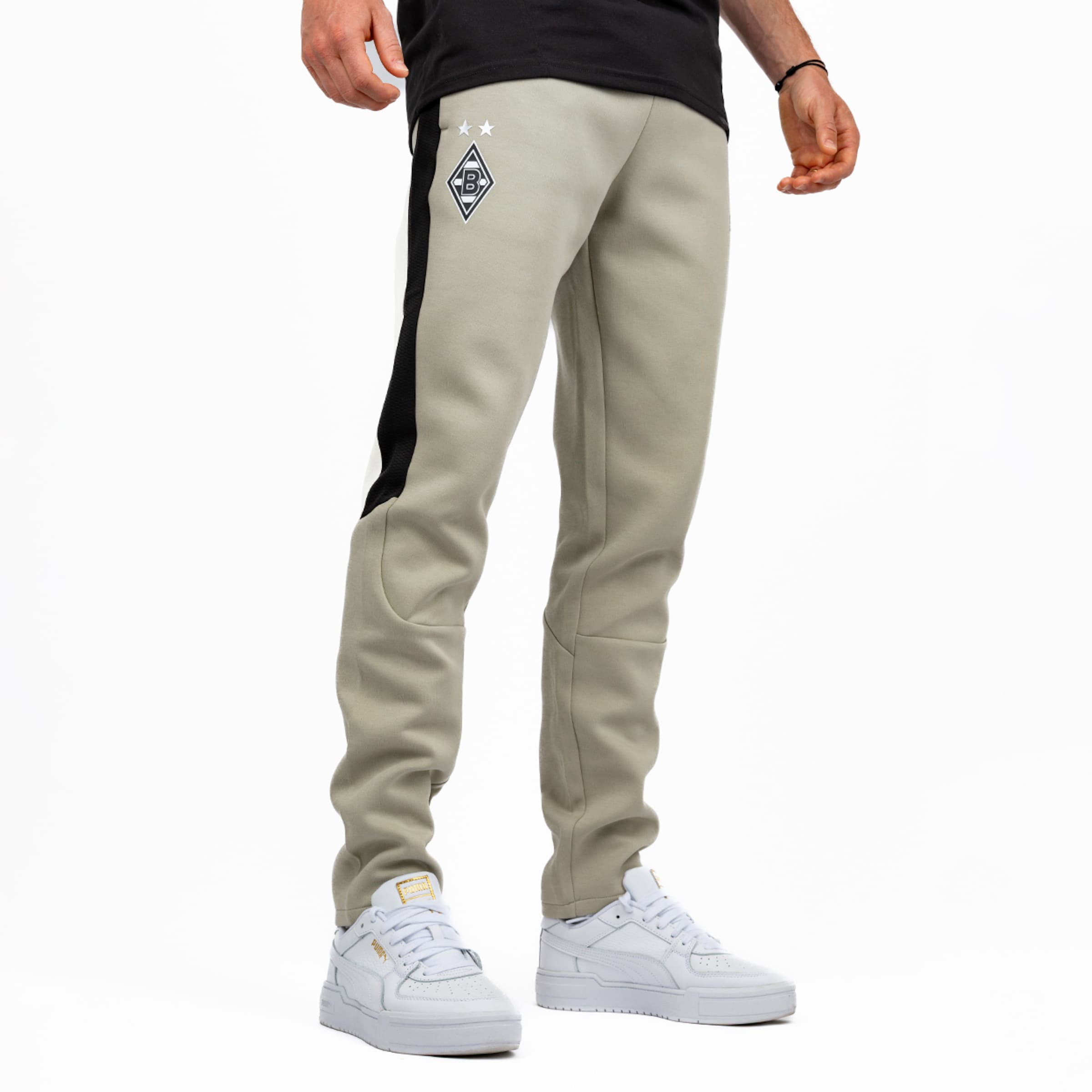 Beige Jogginghose mit schwarzem Seitenstreifen und Borussia Mönchengladbach-Logo mit zwei Sternen am linken Oberschenkel, getragen von einer Person zu einem schwarzen T-Shirt und weißen Sneakern.