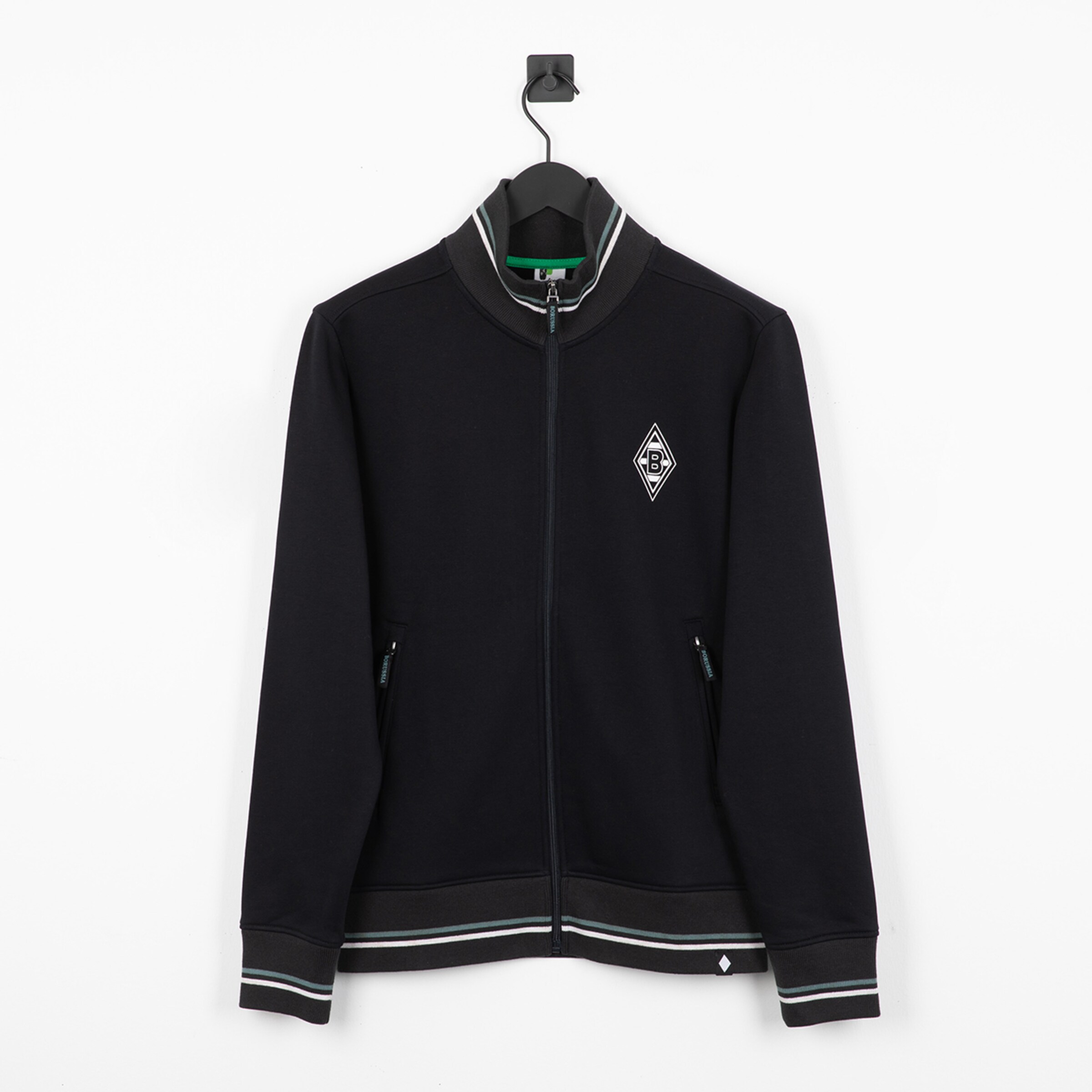 Schwarze Trainingsjacke von Borussia Mönchengladbach mit Logo, Stehkragen und grün-weißen Streifen an Saum und Ärmeln. Auf schwarzem Bügel.