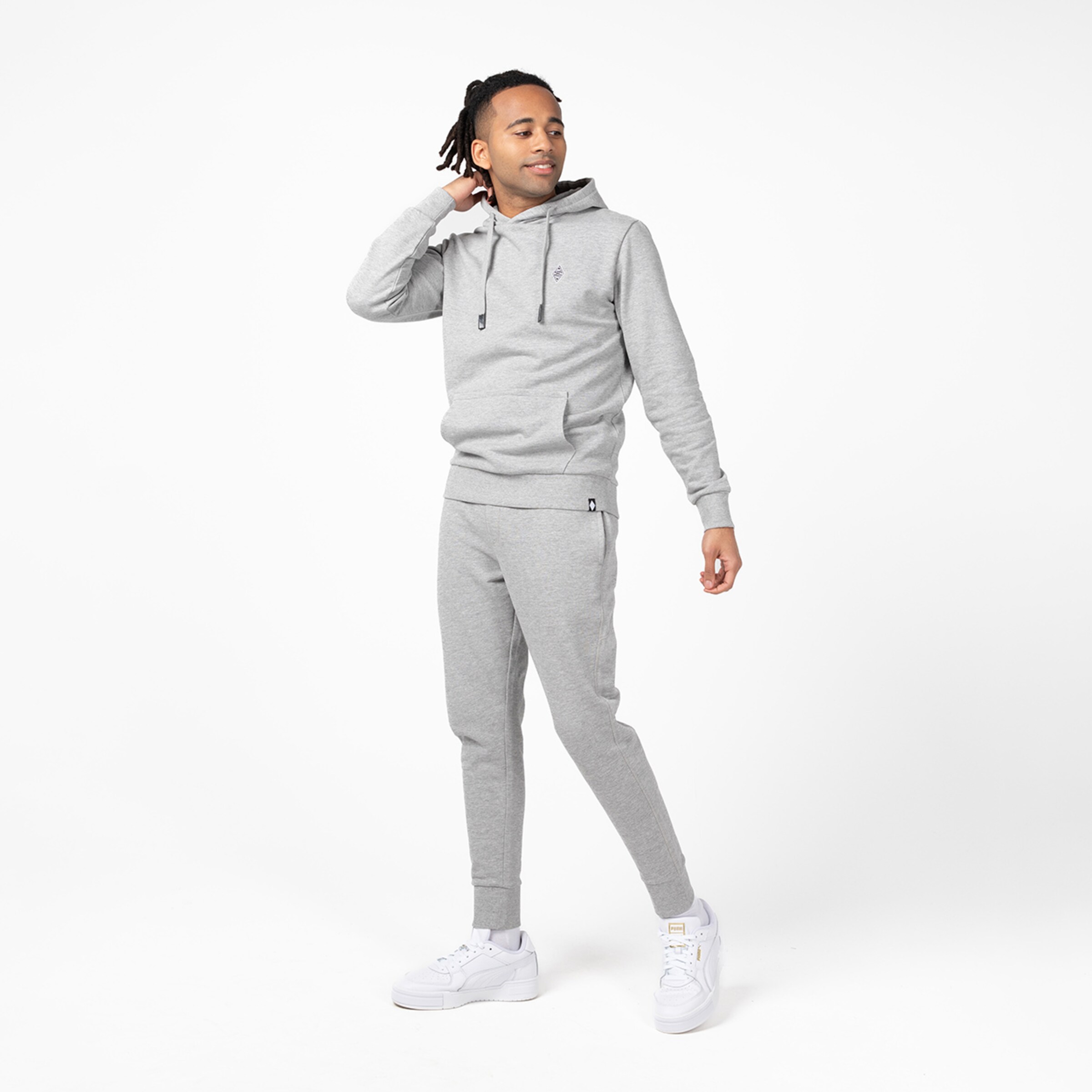 Mann in grauem Sweatsuit mit Kapuze und weißen Sneakers.