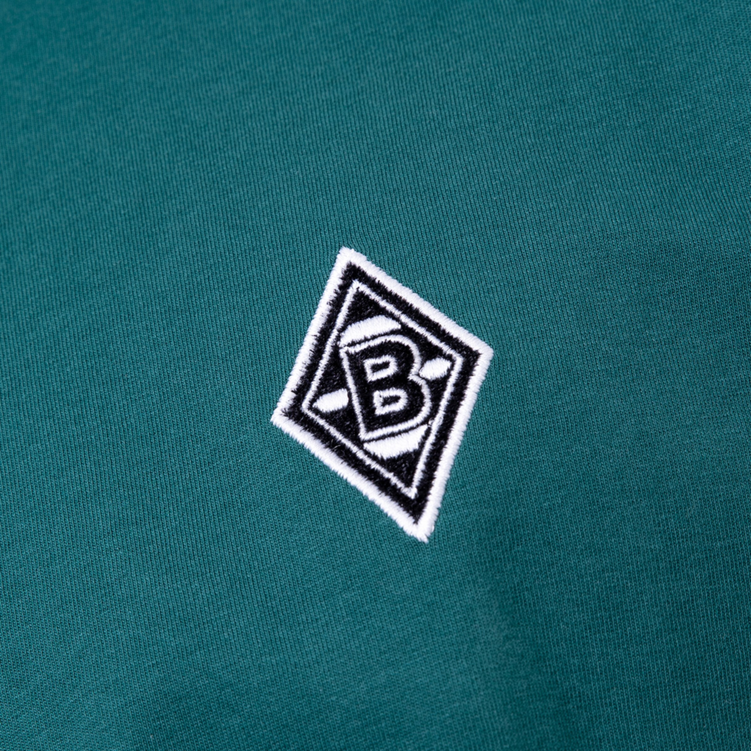 Logo von Borussia Mönchengladbach in schwarzem und weißem Design auf grünem Stoff.