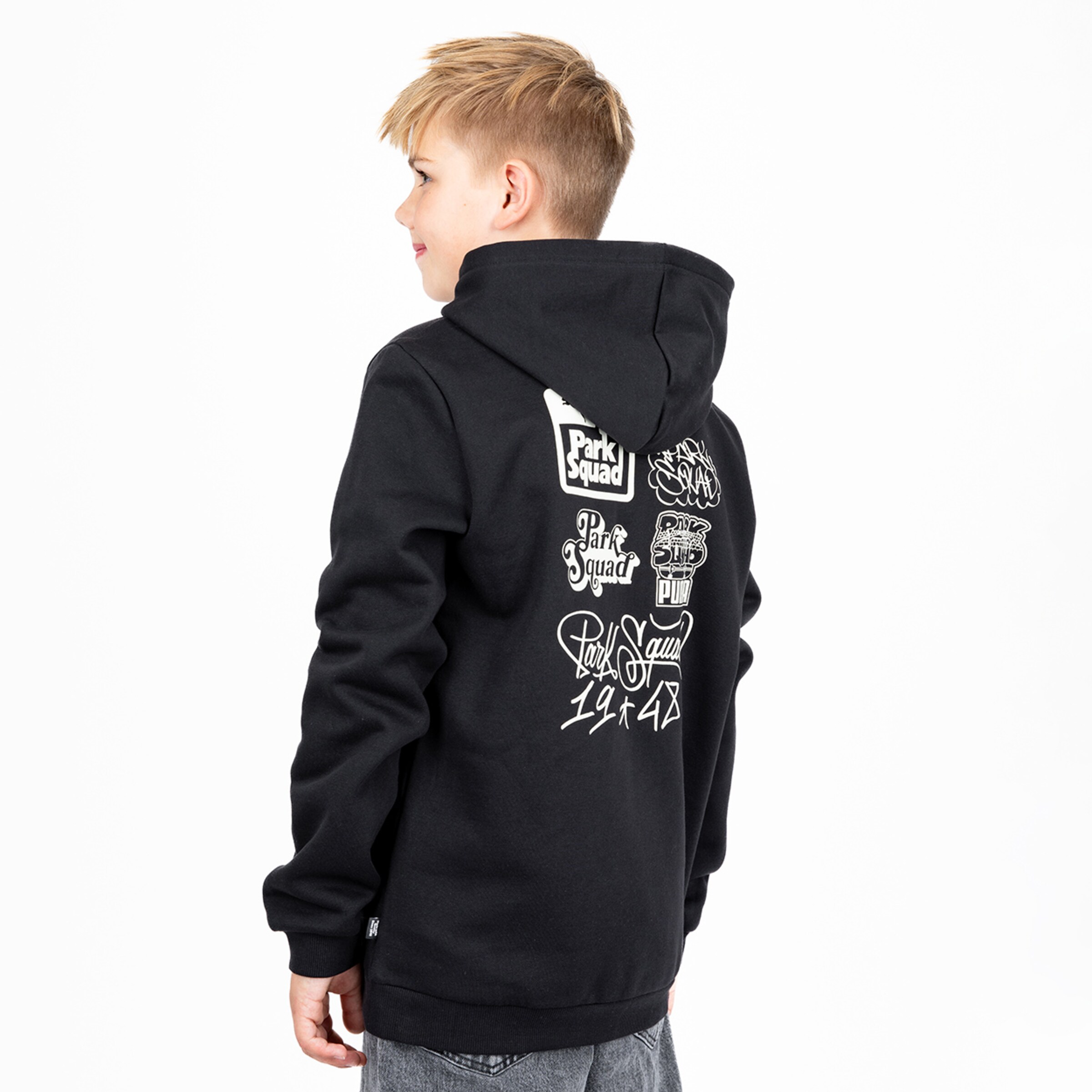 A blonde boy from behind in a black hoodie with white graphic logos on the back against a white background.