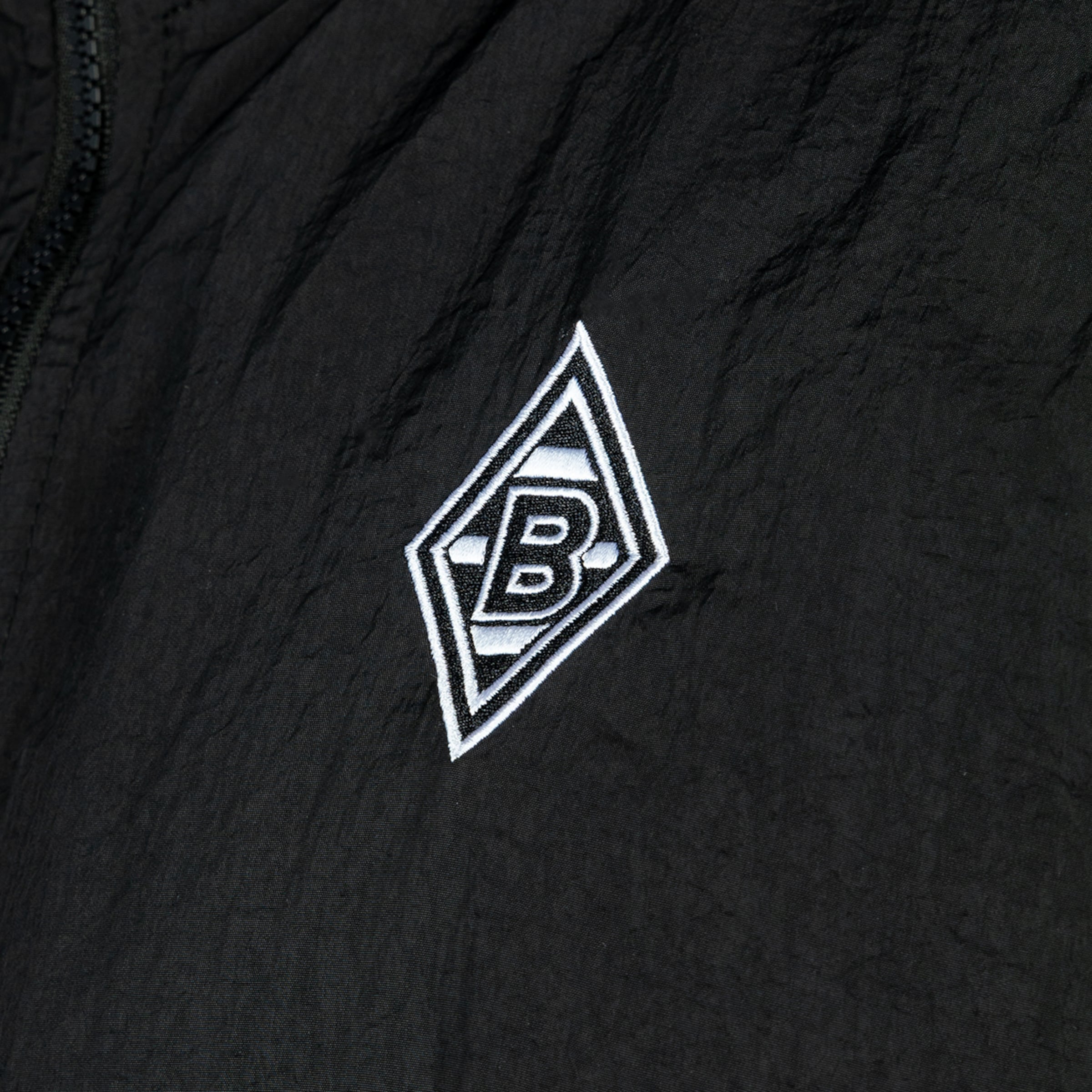 Gesticktes Logo von Borussia Mönchengladbach (weiß-schwarze Raute mit „B“) auf schwarzem, strukturiertem Stoff.