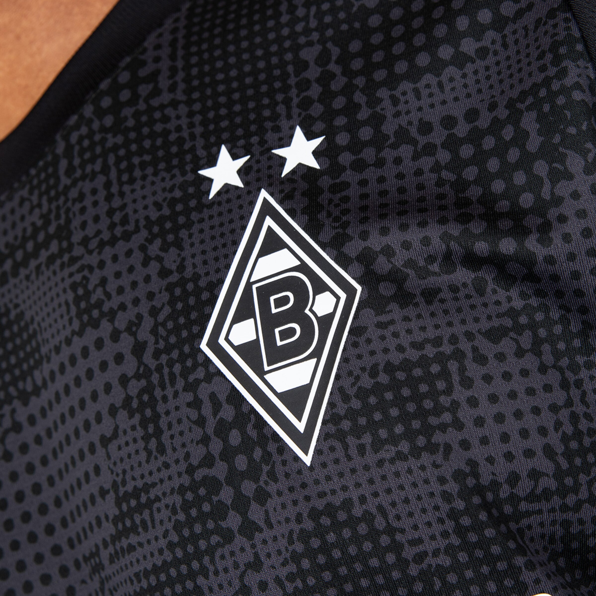 Das Vereinswappen von Borussia Mönchengladbach mit zwei Sternen darüber auf einem sportlichen Trikot.