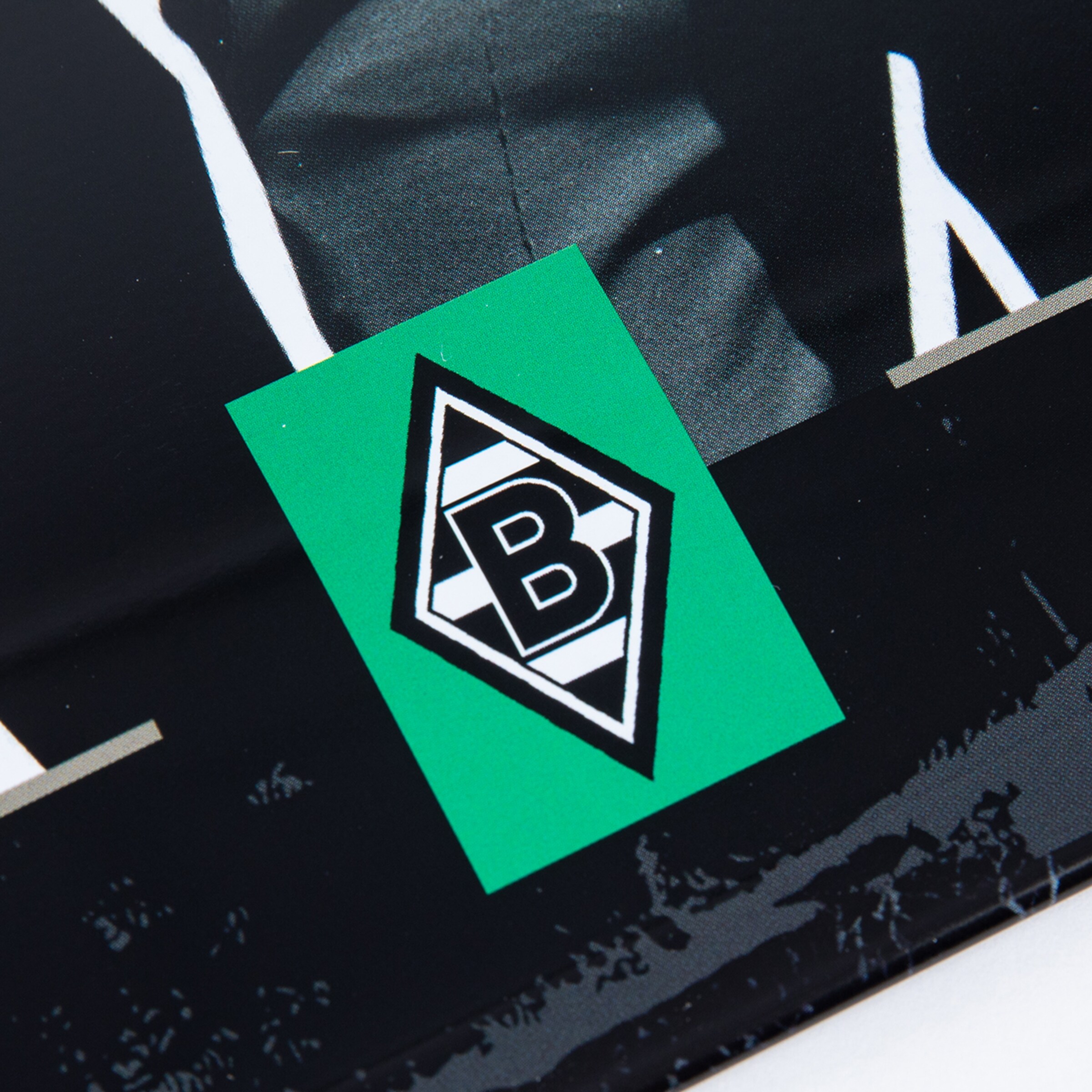 Grüner Sticker mit dem schwarz-weißen Rauten-Logo von Borussia Mönchengladbach (Buchstabe B) auf einer schwarzen, glänzenden Oberfläche.
