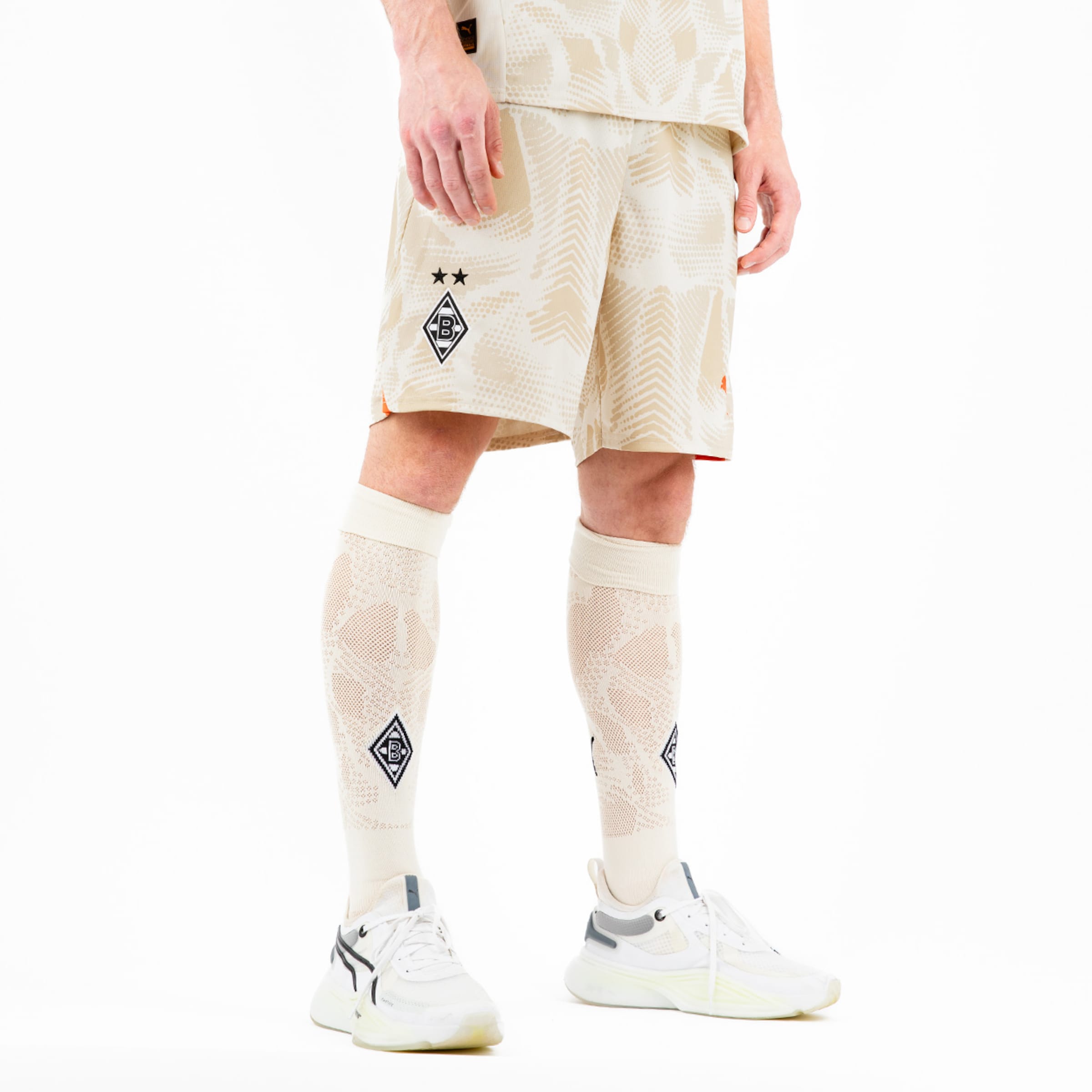 Ein männlicher Fußballspieler trägt eine beige Trikot-Hosen-Kombination mit zwei Sternen und passenden Schienbeinschonern.