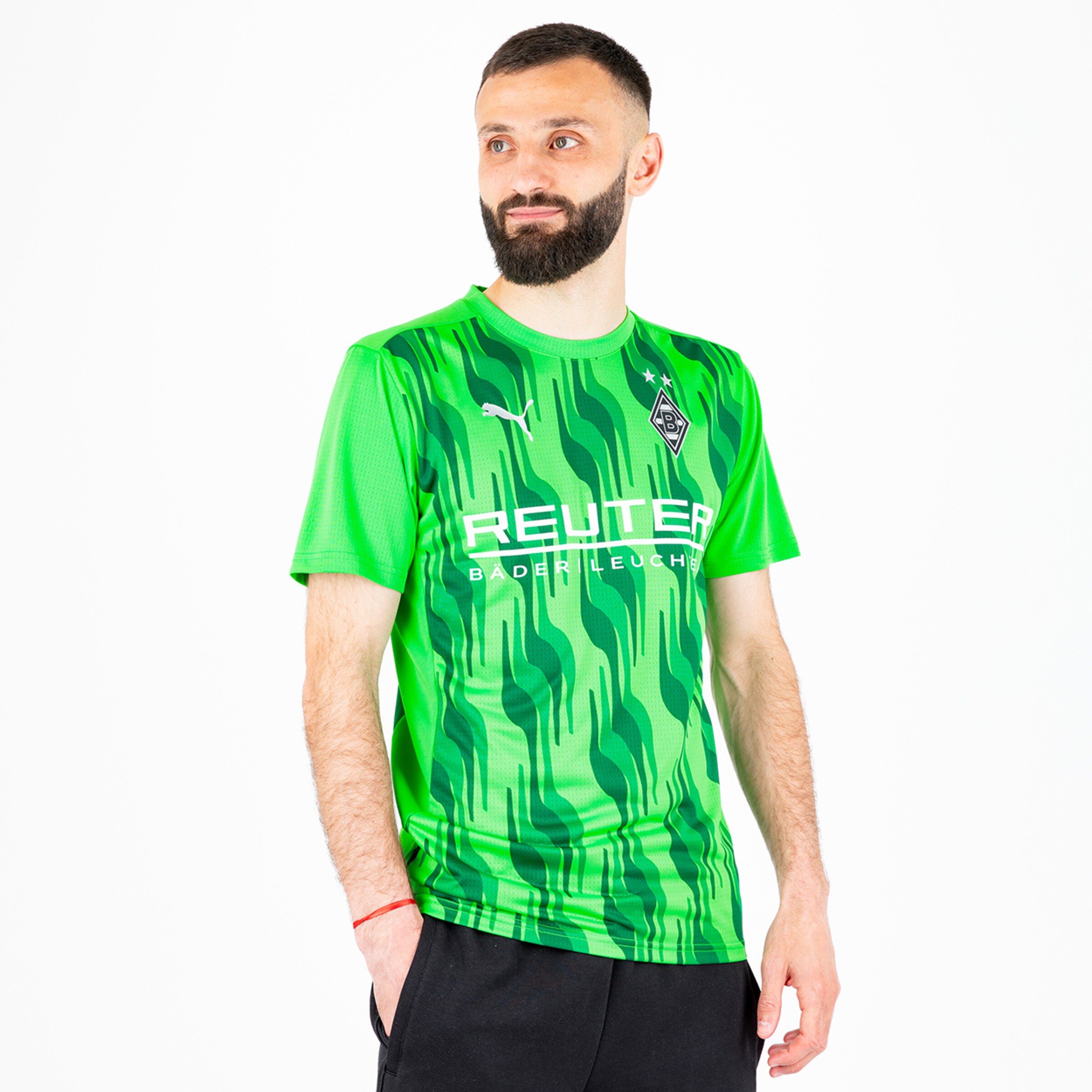 Ein männliches Model trägt ein grünes Fußballtrikot mit einem dynamischen Muster und dem Logo von Borussia Mönchengladbach.