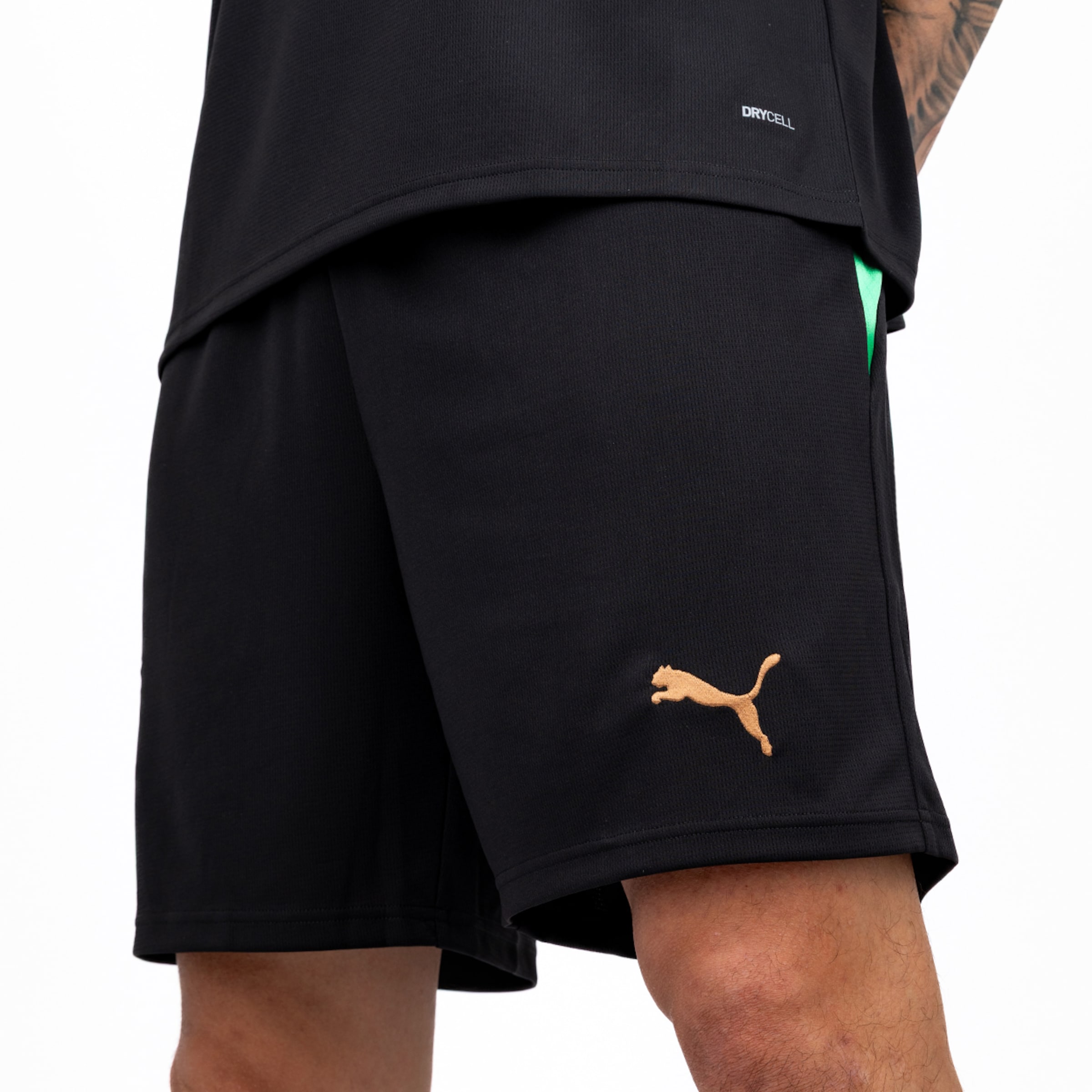 Black Puma shorts with a gold logo and green detail, paired with a black Drycell shirt on a white background.