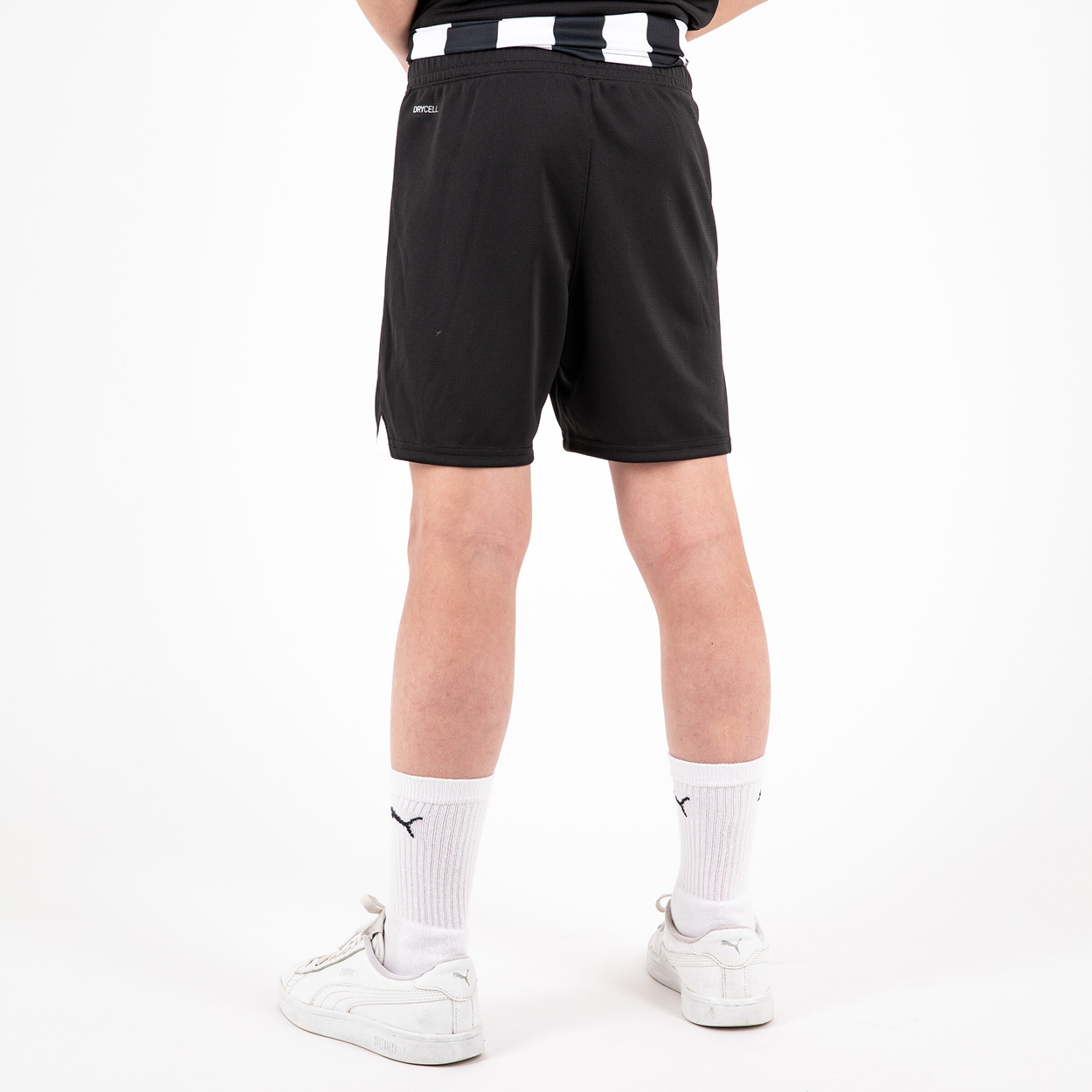 Back view of a child wearing black sports shorts and white socks with black sneakers.