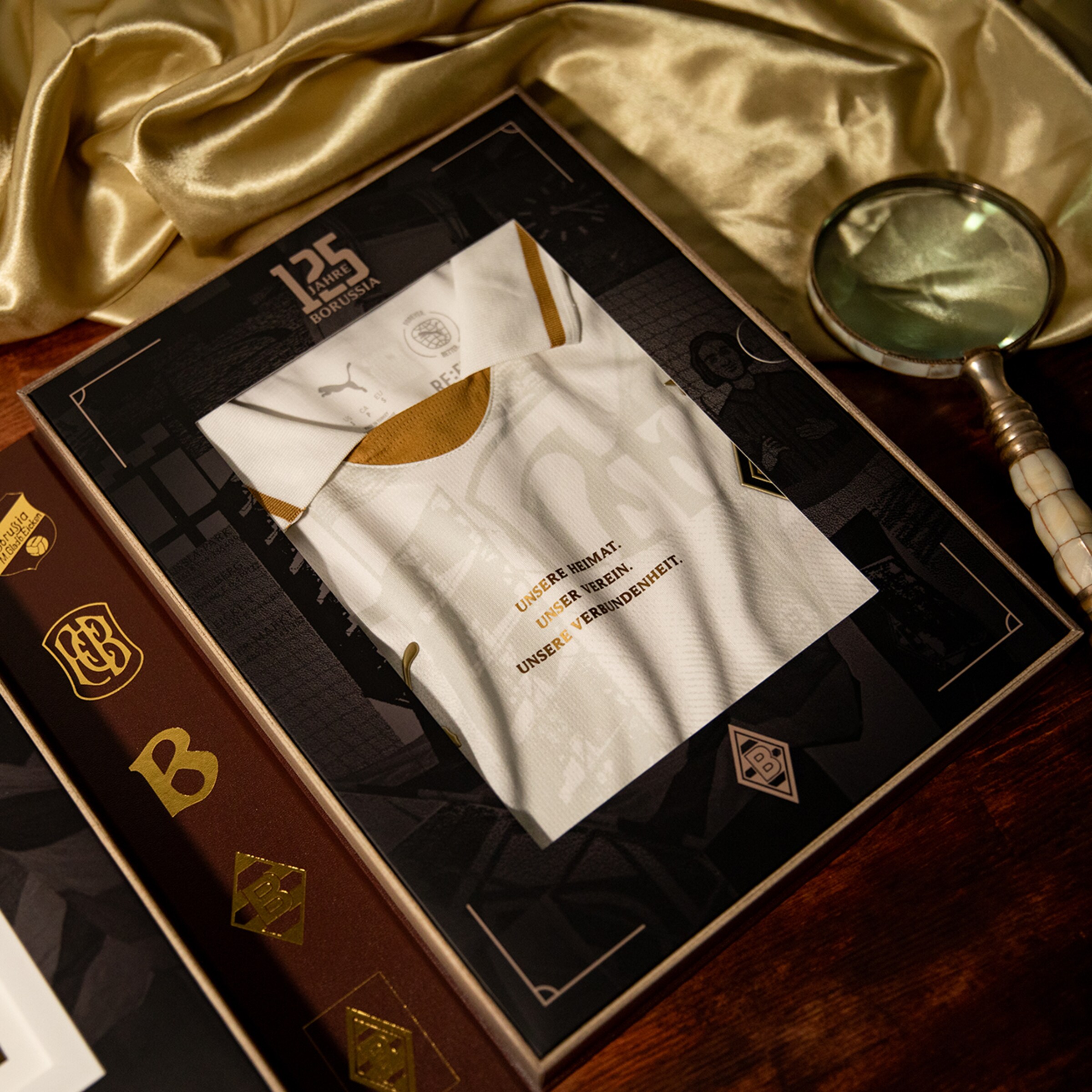 Borussia Mönchengladbach Jubiläumstrikot zum 125. Bestehen in edler Box mit Gold-Akzenten und Lupe auf goldenem Seidenstoff.