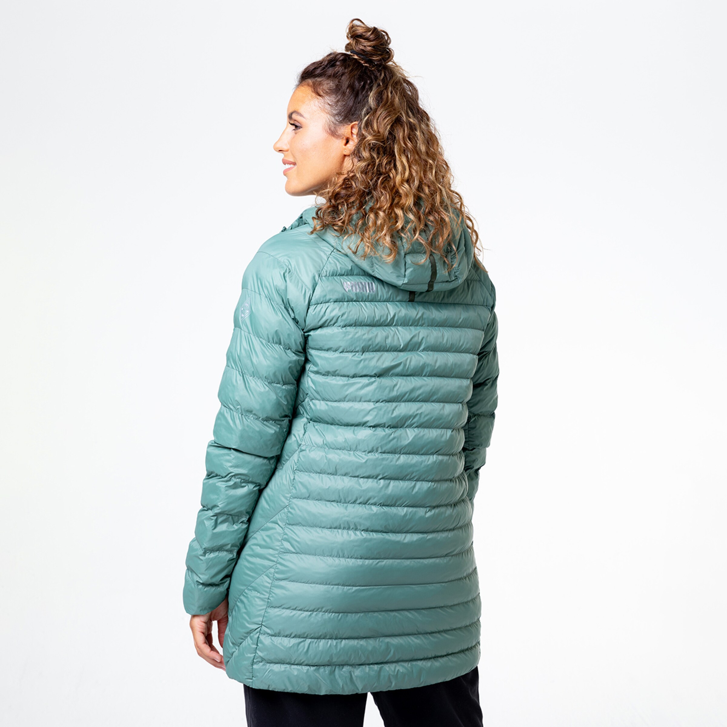 Frau mit lockigem Haar trägt eine grüne gepolsterte Jacke und schaut über die Schulter.