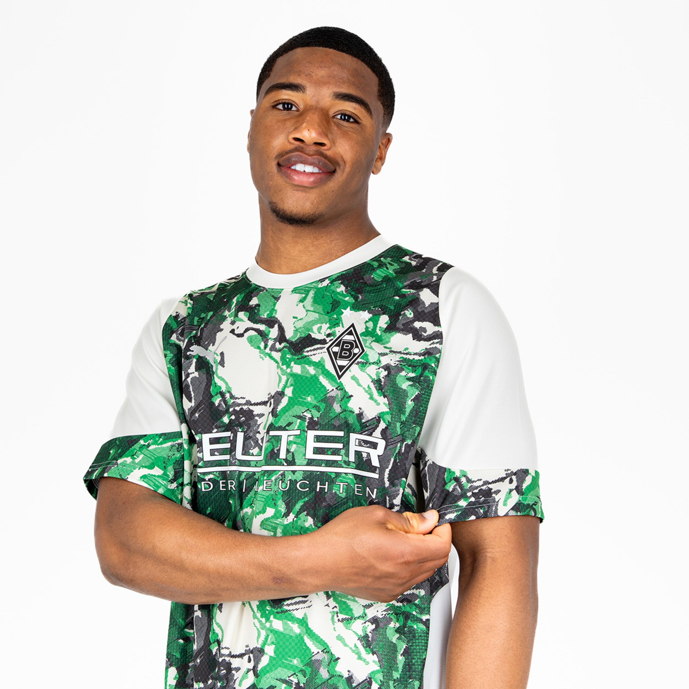 Ein Fußballspieler in einem T-Shirt mit grünem camouflagemuster und dem Schriftzug ELTER