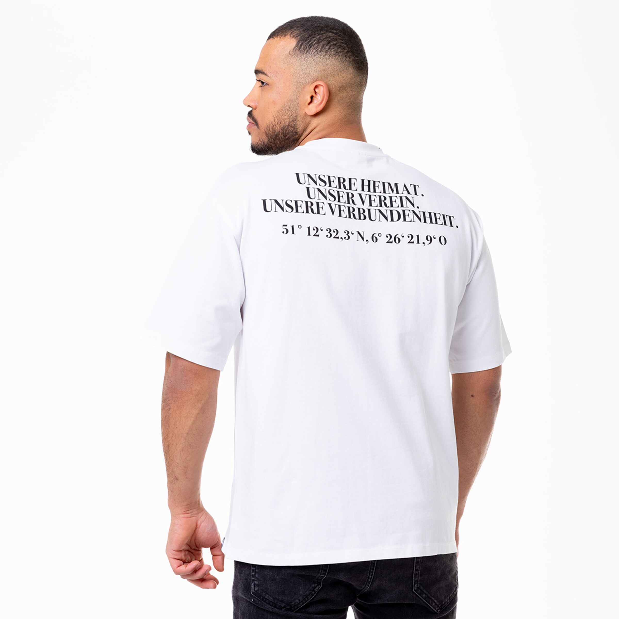 Mann mit T-Shirt auf dem die Aufschrift UNSERE HEIMAT. UNSER VEREIN. UNSERE VERBUNDENHEIT. zu sehen ist steht seitlich zum Betrachter.
