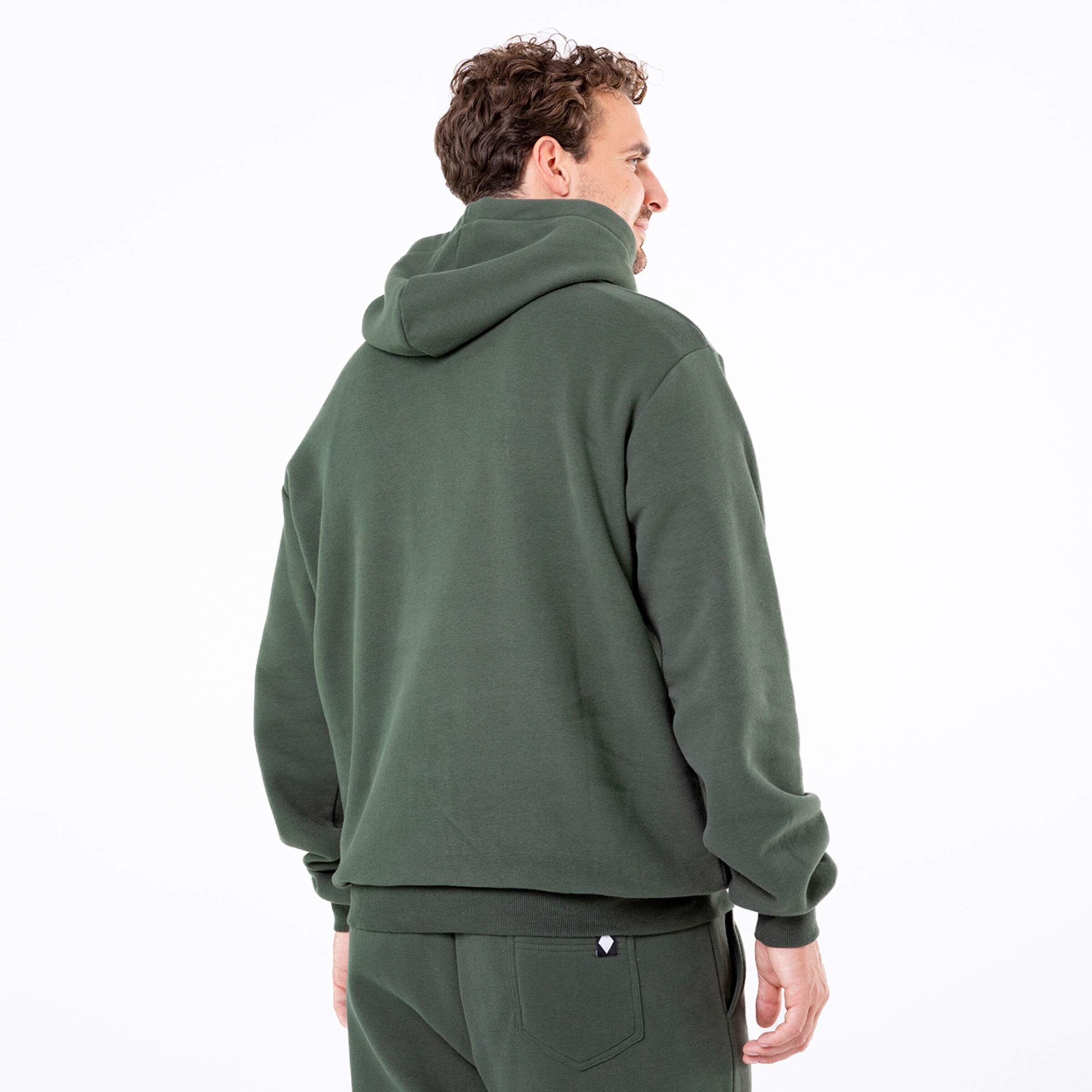 Ein Mann mit lockigen Haaren trägt einen grauen Kapuzenpullover und schaut über seine Schulter.