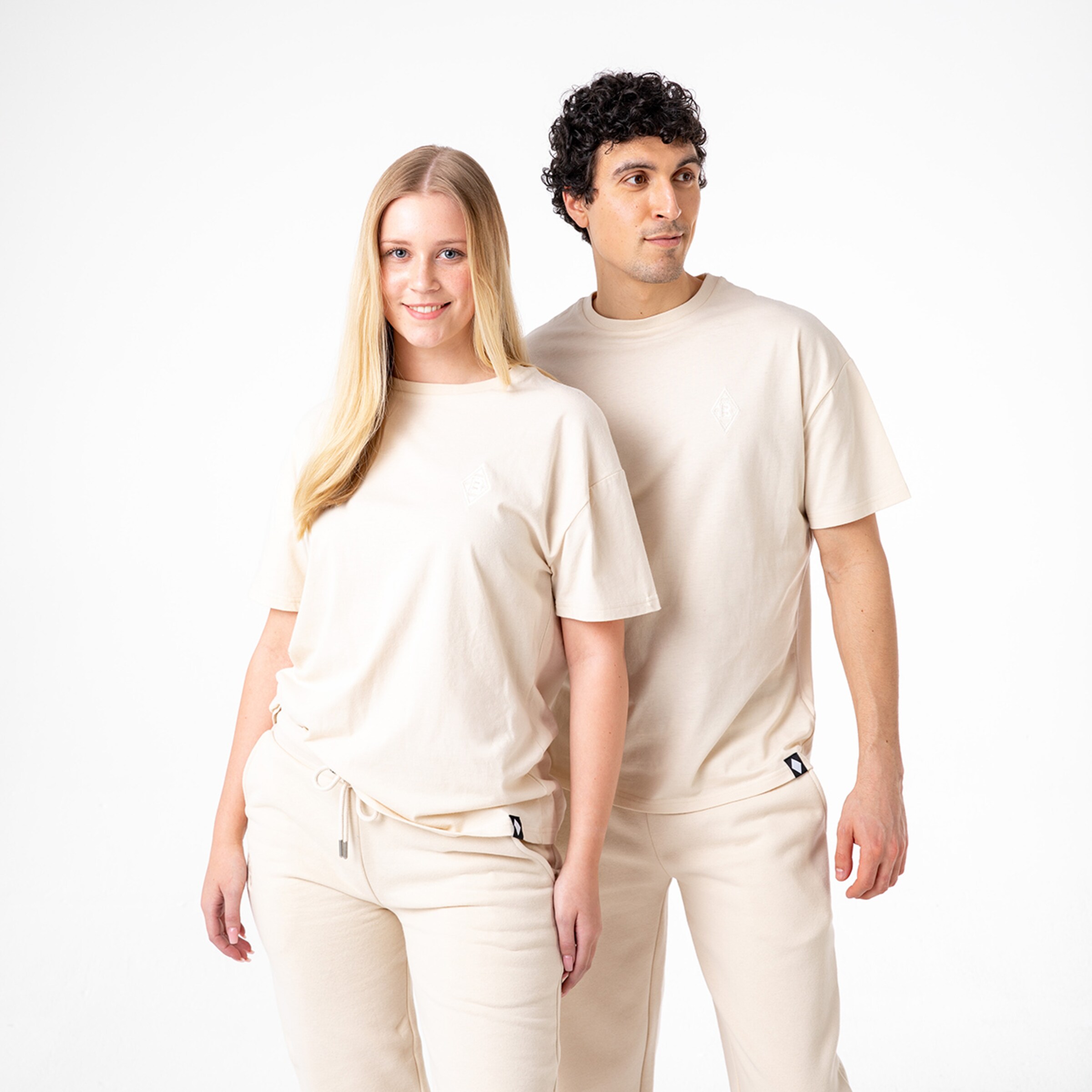 Ein Mann und eine Frau posieren in beiger Freizeitkleidung mit kurzen Ärmeln und lässiger Passform.