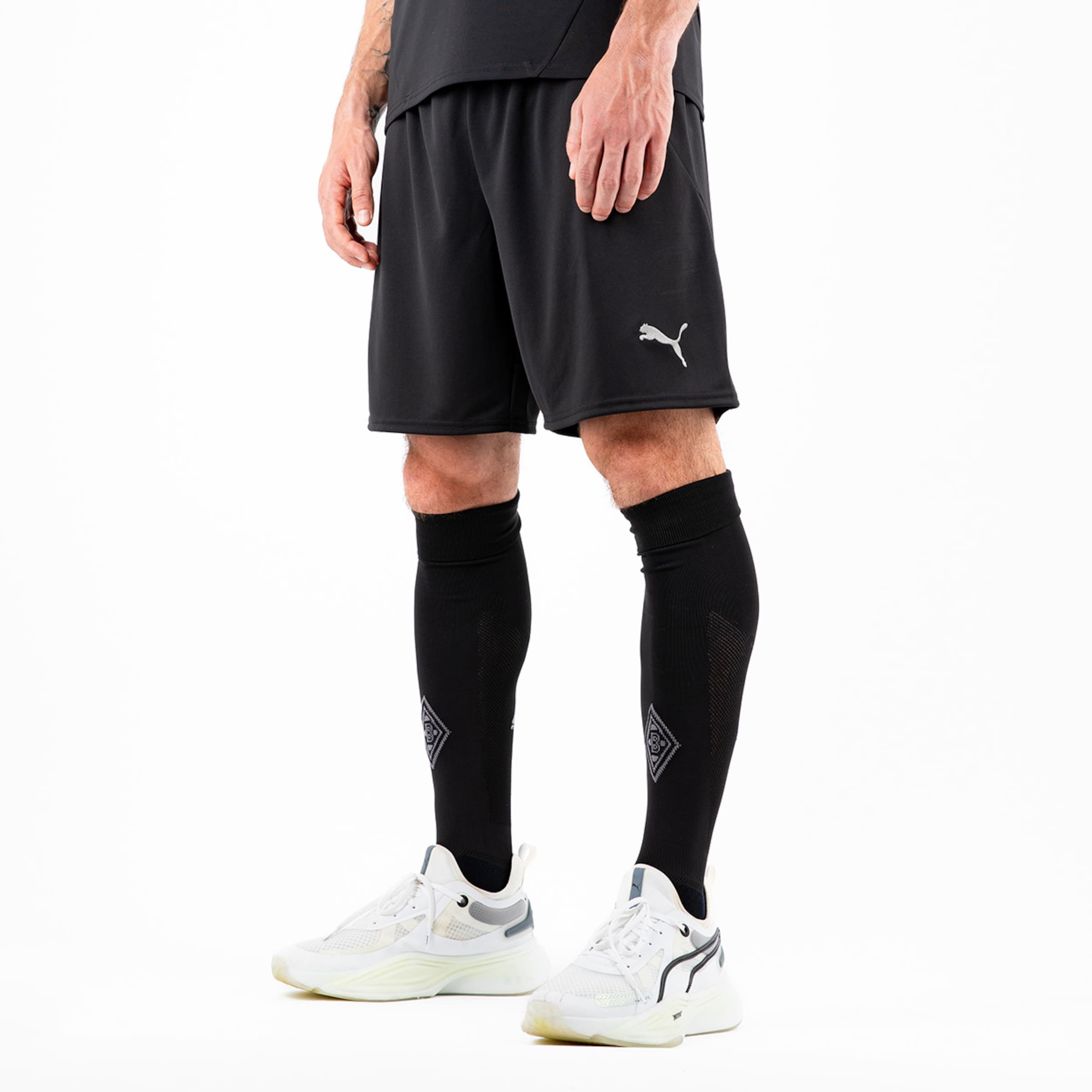 Sportliche schwarze Shorts von Puma mit langen schwarzen Stulpen und weißen Schuhen.