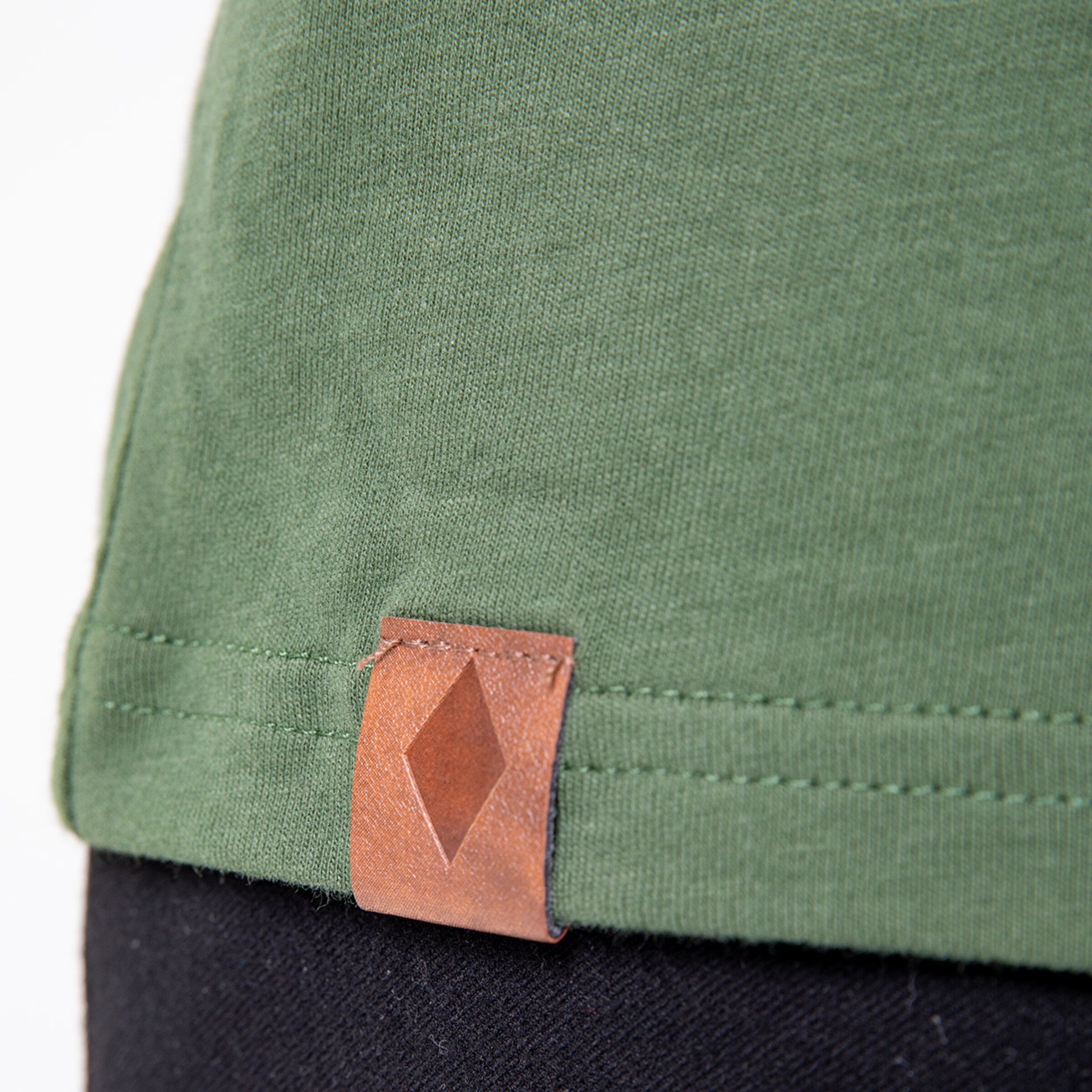 Detailansicht eines grünen T-Shirts mit Lederlabel am Saum.