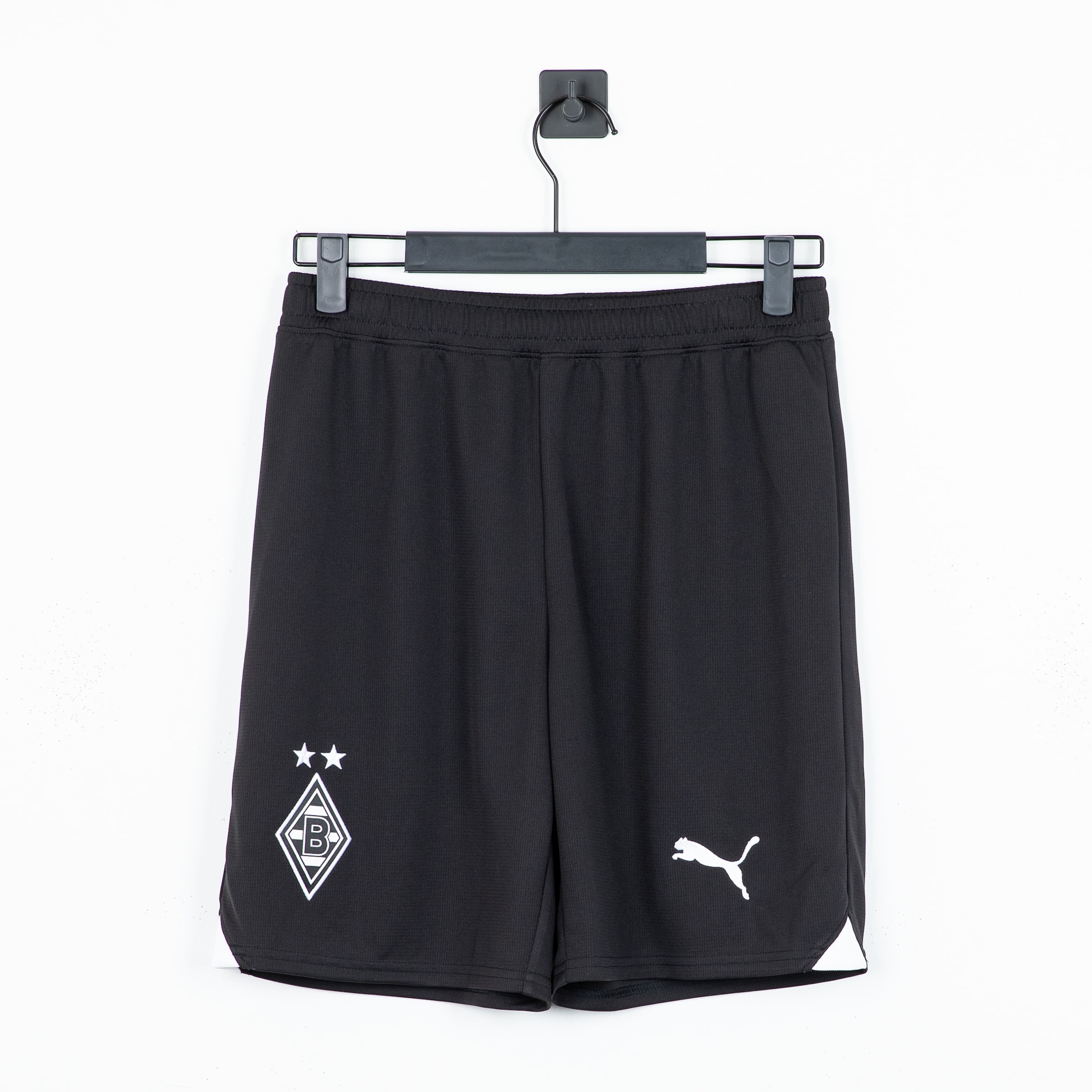 Schwarze Puma Borussia Mönchengladbach Fußballshorts auf einem Bügel mit weißem Vereinswappen und Puma-Logo vor weißem Hintergrund.