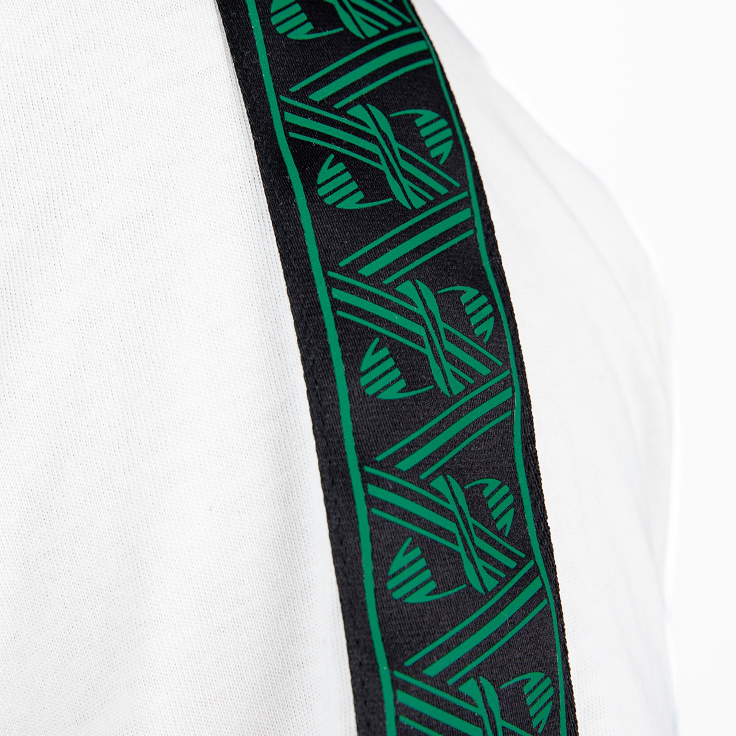 Detailansicht eines weißen Oberteils mit schwarzem Zierstreifen, der ein wiederkehrendes grünes Grafikmuster zeigt.