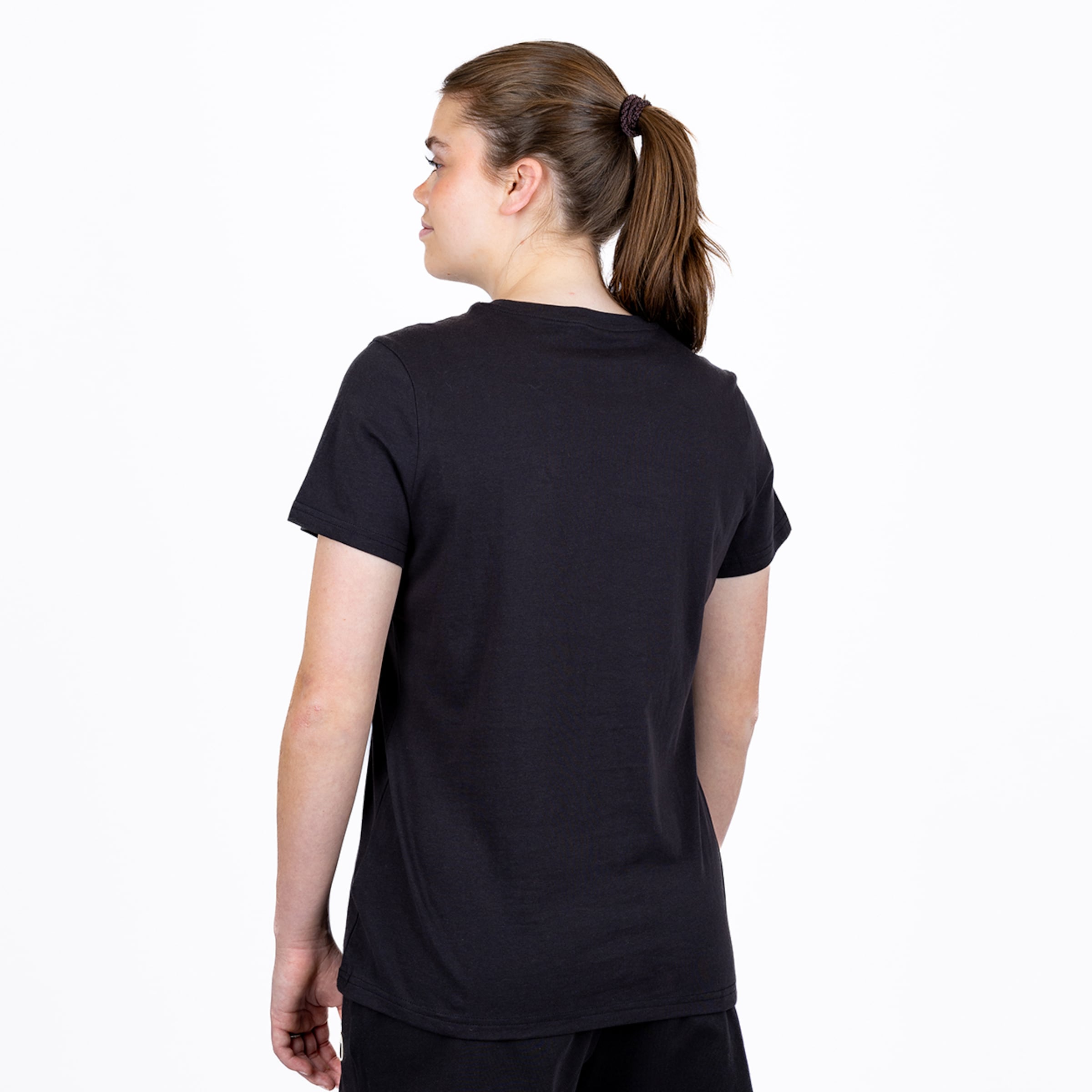 Rückansicht einer Frau mit Pferdeschwanz in einem schlichten schwarzen Kurzarm-T-Shirt vor weißem Hintergrund.