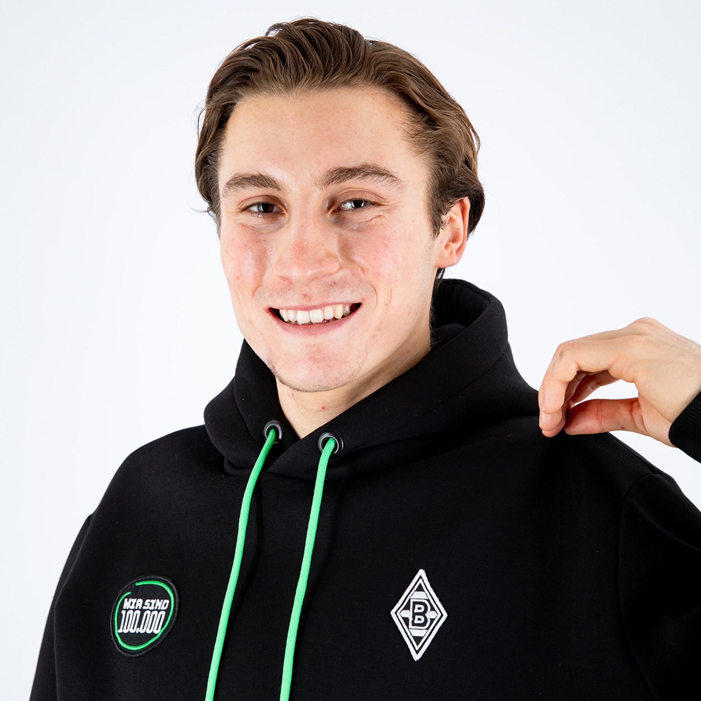 Junger Mann mit leichtem Lächeln trägt einen schwarzen Hoodie mit einem Borussia Mönchengladbach-Logo.