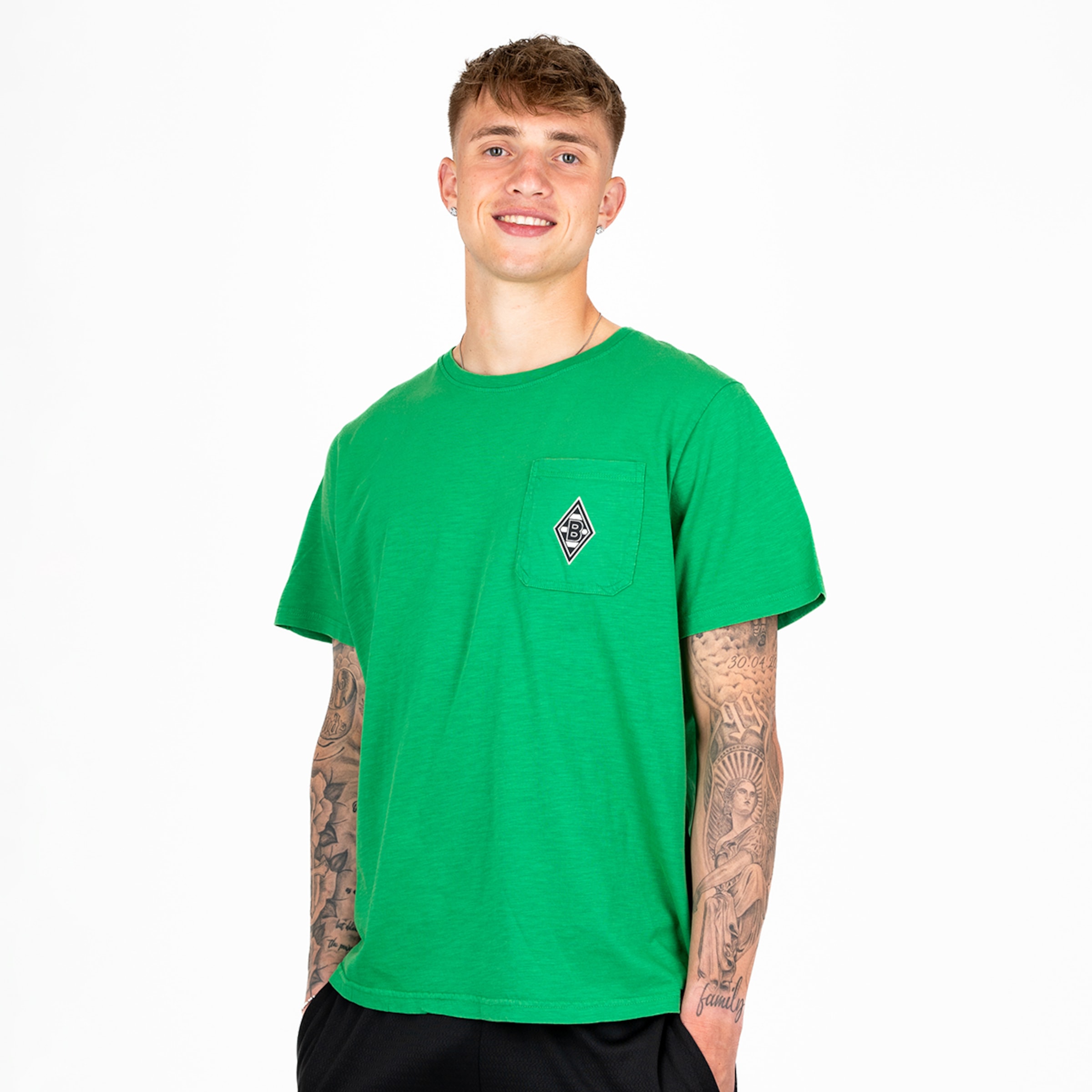 Junger Mann trägt ein grünes T-Shirt mit einem kleinen Aufdruck auf der Brust.