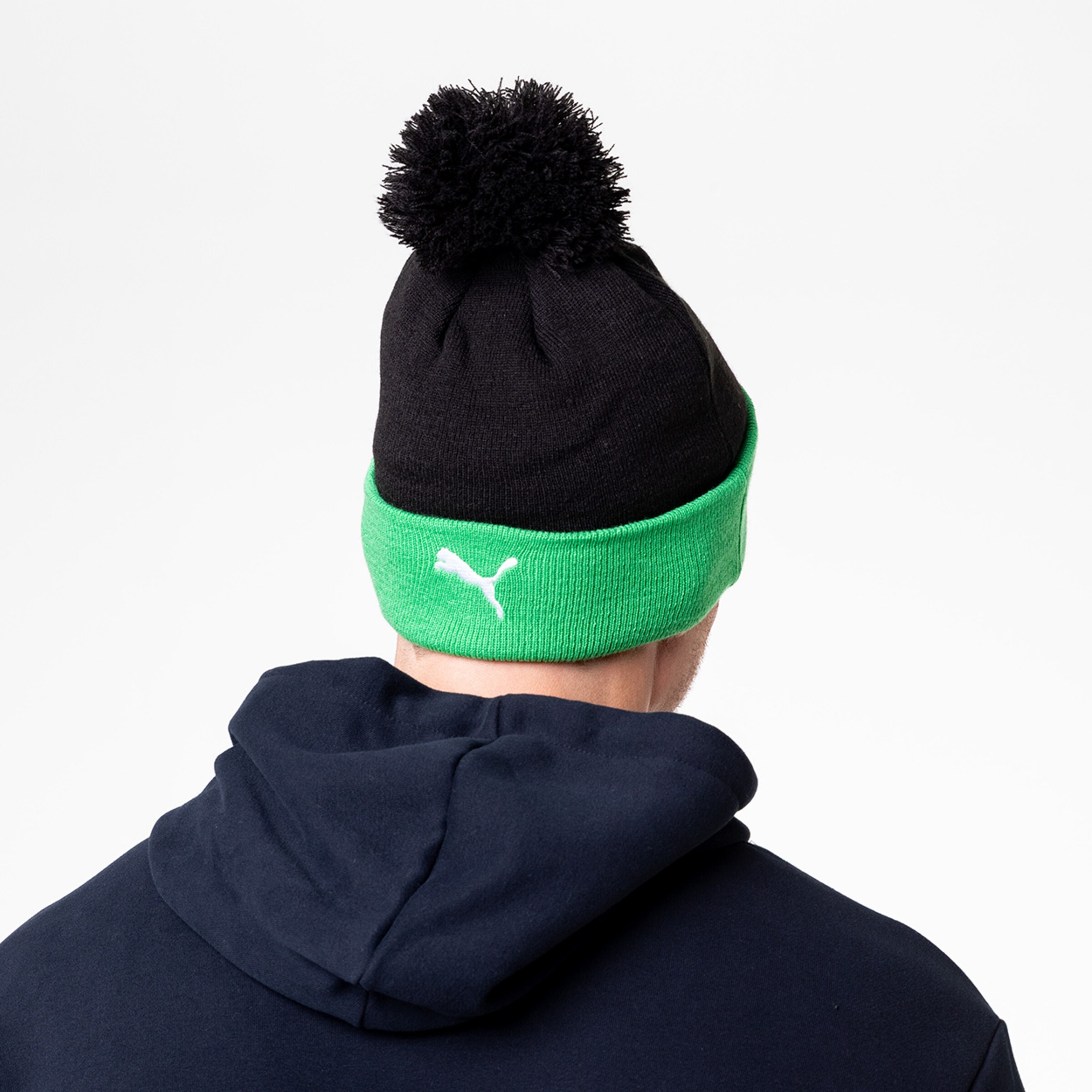 Schwarze Mütze mit grüner Kante und Bommel von der Rückseite gesehen.