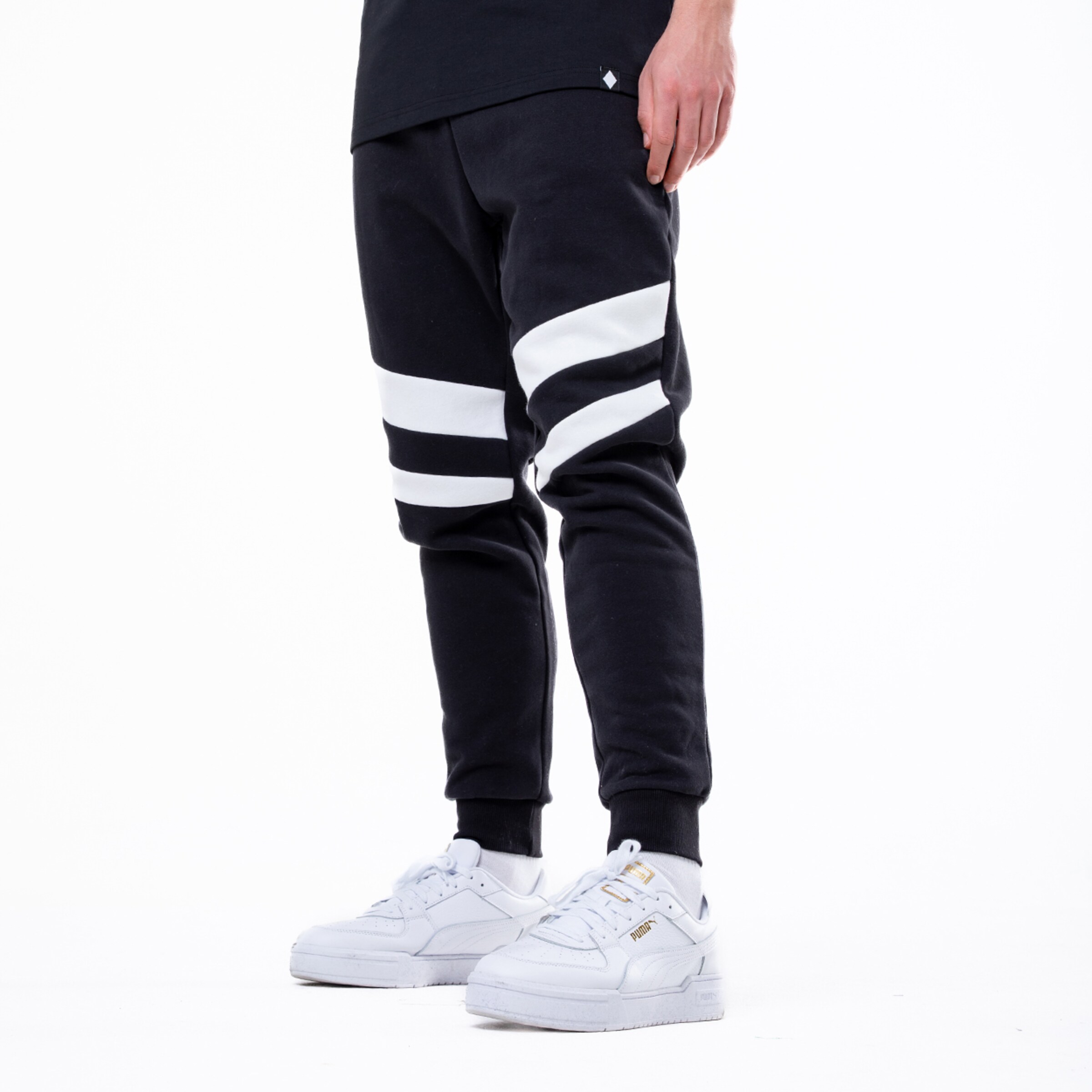 Person in schwarzer Jogginghose mit markanten weißen Streifen und weißen Puma-Sneakern vor weißem Hintergrund.