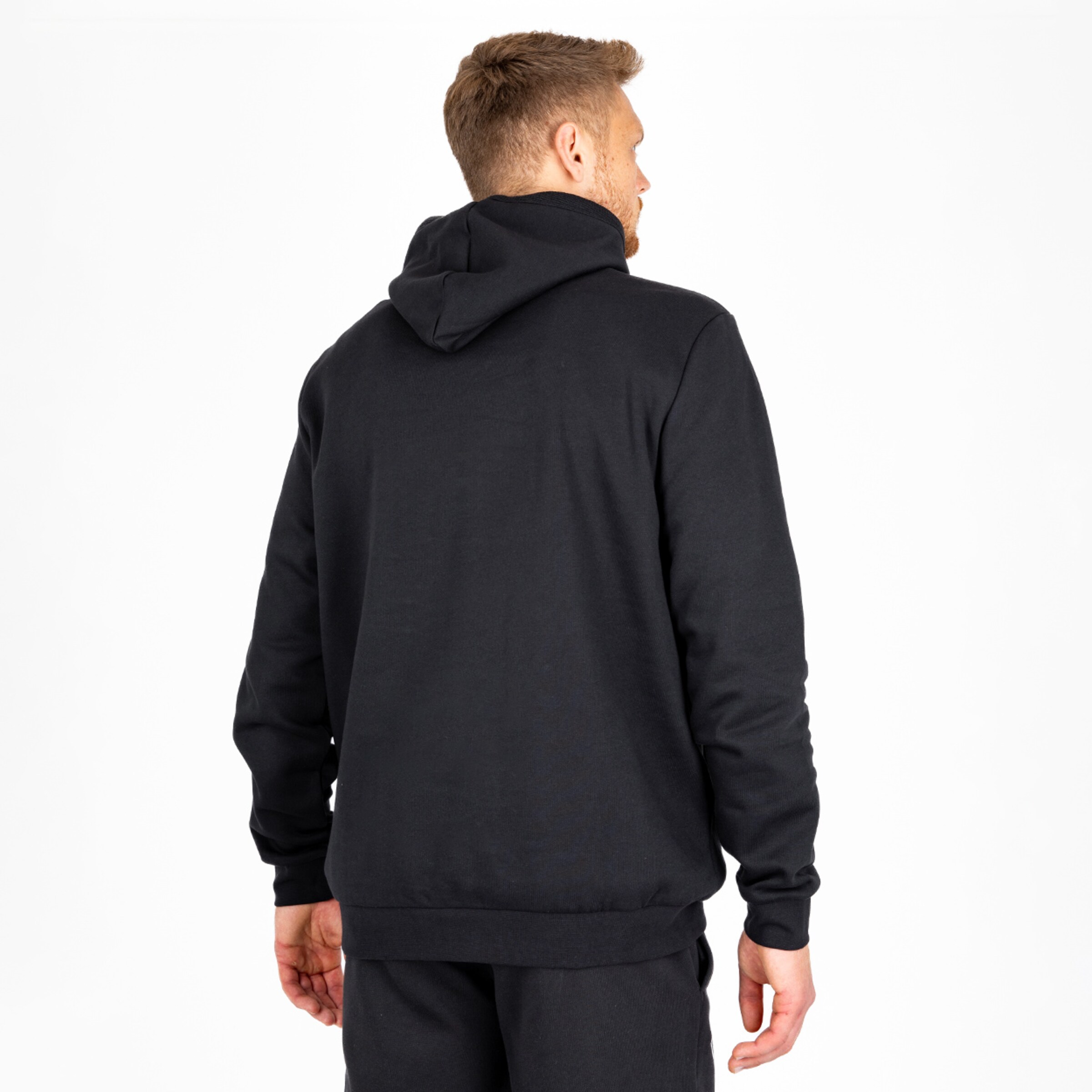 Mann im schwarzen Hoodie von hinten gesehen steht aufrecht.