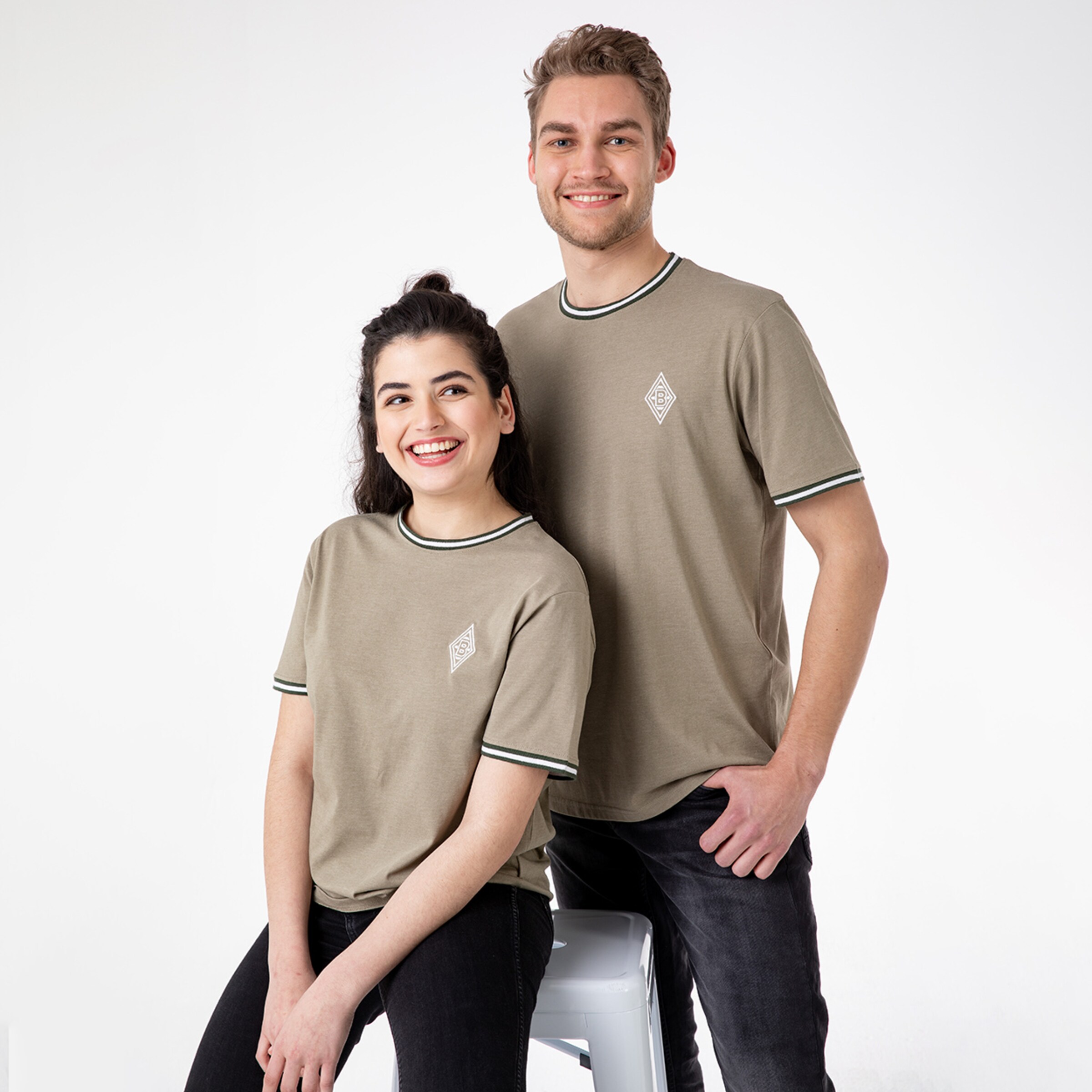Two people pose in neutral T-shirts with green trim and a logo on the chest.