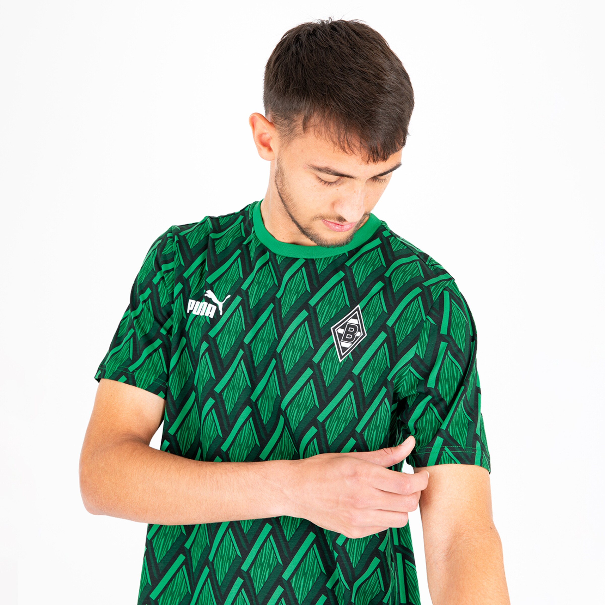 Ein junger Mann trägt ein grünes Trikot mit einem geometrischen Muster und untersucht seinen Ärmel.