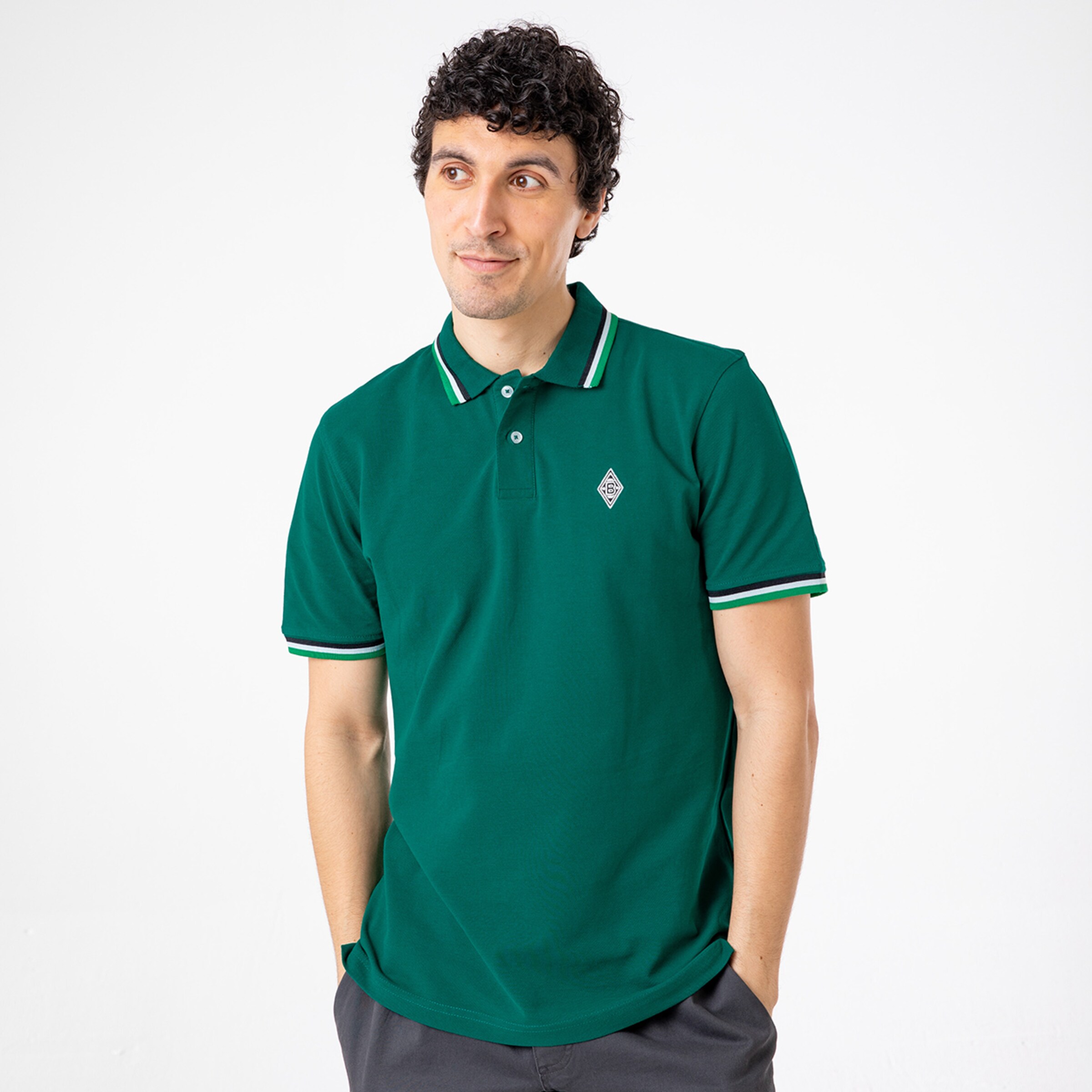 Mann trägt ein grünes Poloshirt mit gestreiften Säumen und einem Vereinslogo.