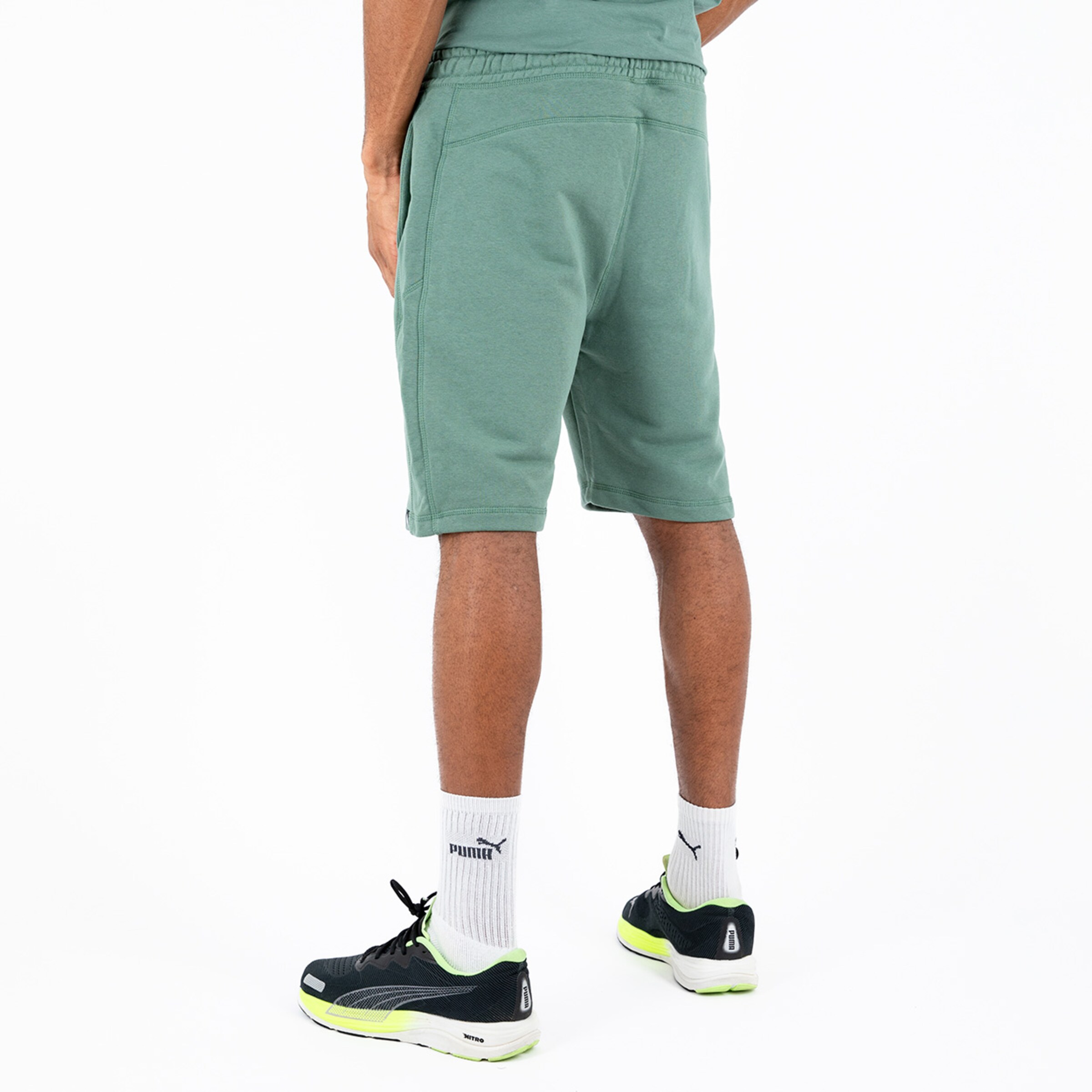 Mann mit grünen Sweatshorts und schwarzen Sportschuhen von hinten fotografiert.