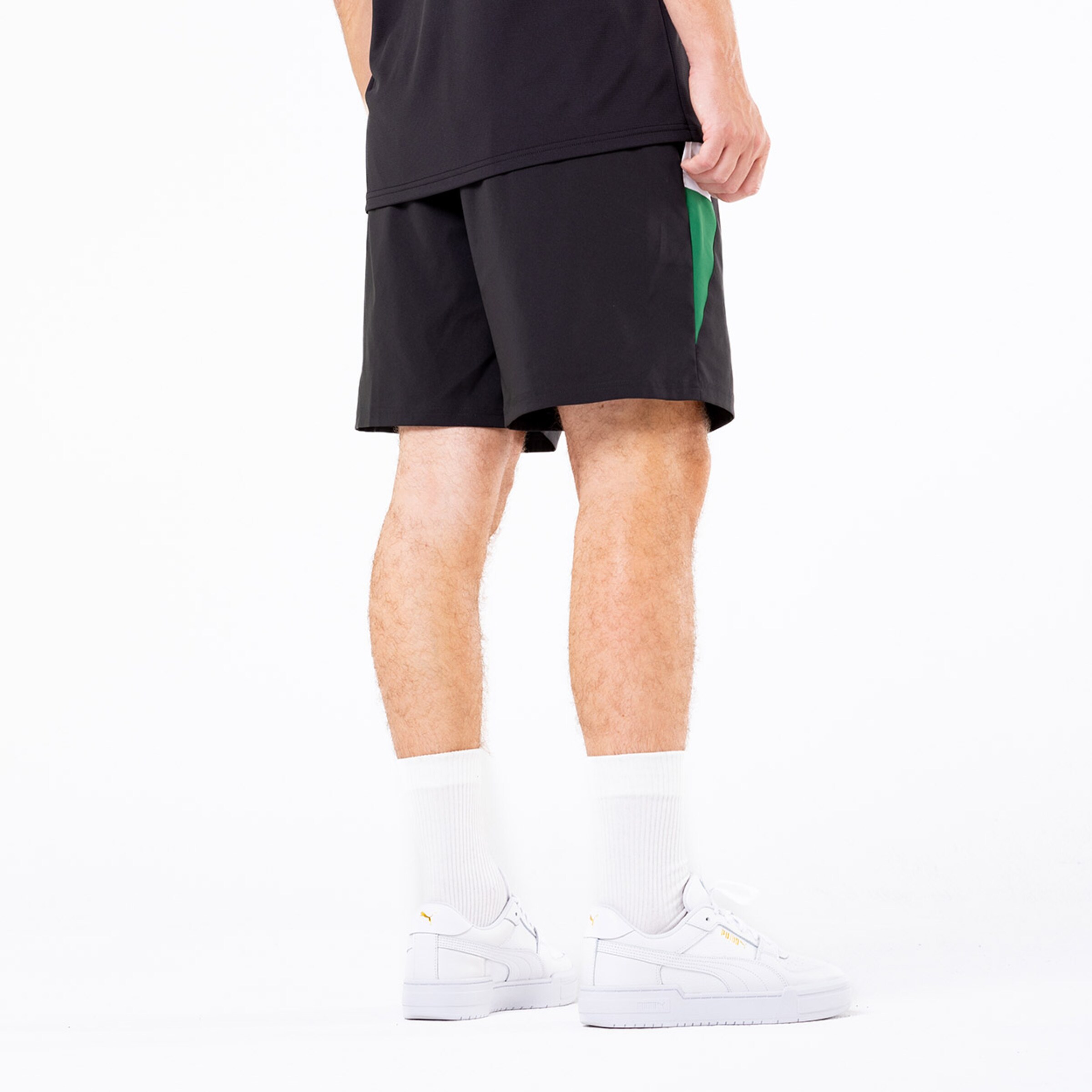 Mann von hinten in kurzen schwarzen Sporthosen mit grünem Detail und weißen Sneakers.