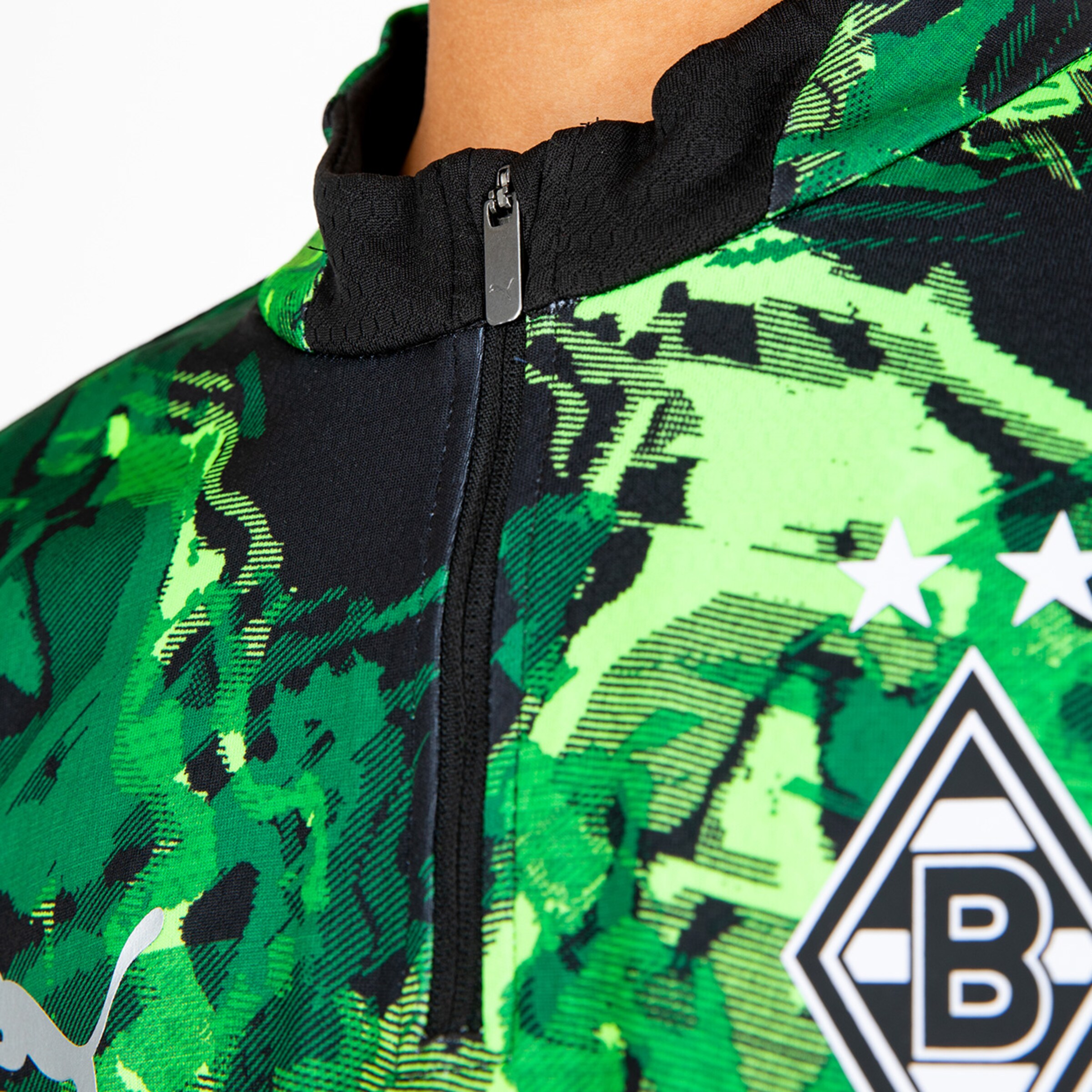 Detailansicht eines Fußballtrikots mit grünem schuppigem Muster und Vereinslogo von Borussia Mönchengladbach.