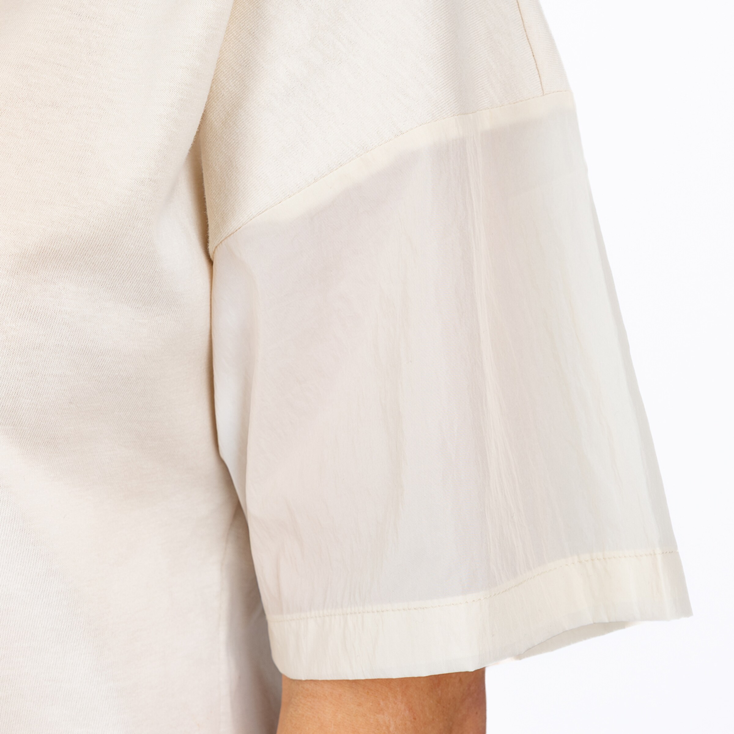 Detailaufnahme eines cremefarbenen Oberteils mit einem Ärmel aus blickdichtem Stoff und einem halbtransparenten Einsatz.