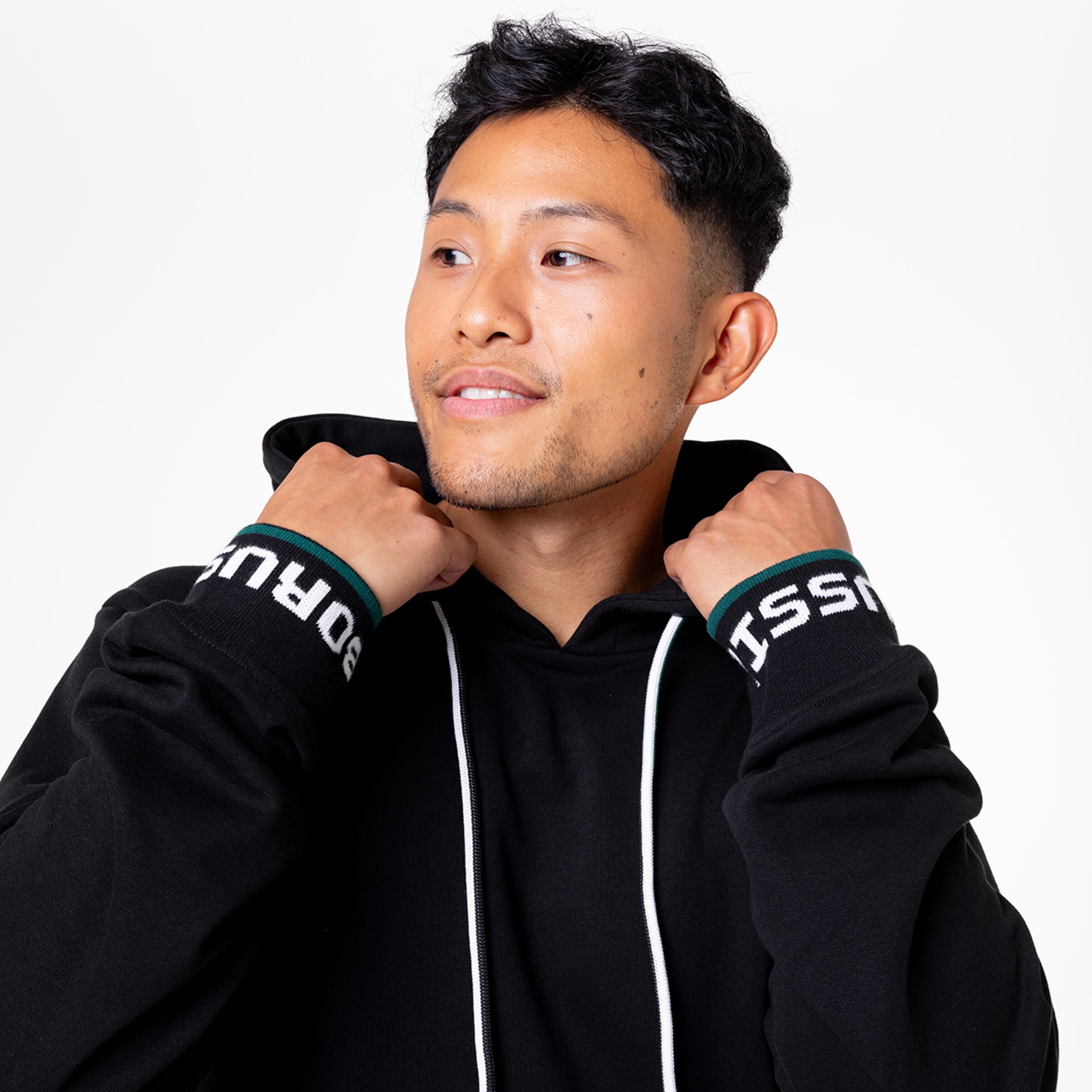 Young man in a casual black hoodie smiling and pulling up the hood.